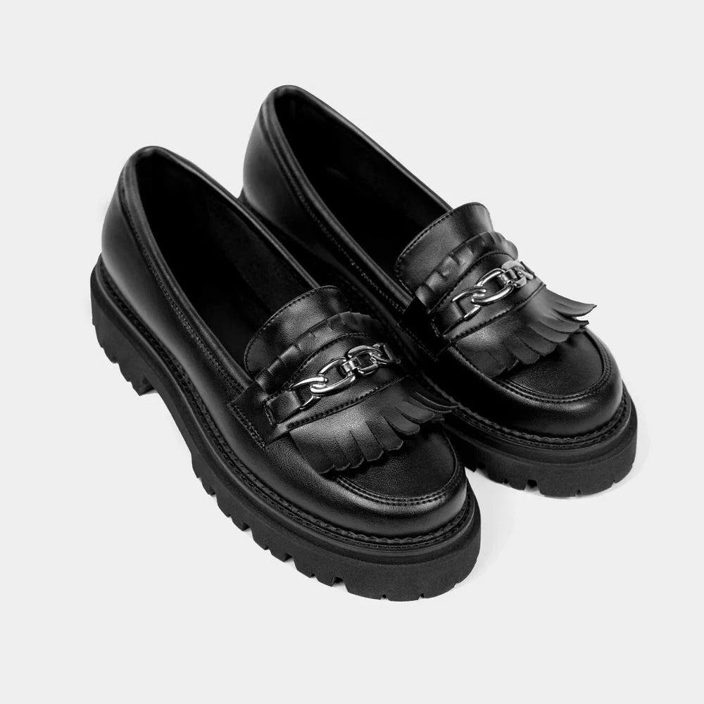 Ein Paar schwarze Leder-Slipper mit klobigen Gummisohlen, dekorativen Fransen auf der Vorderseite und einem silbernen Kettendetail auf dem Schaft.