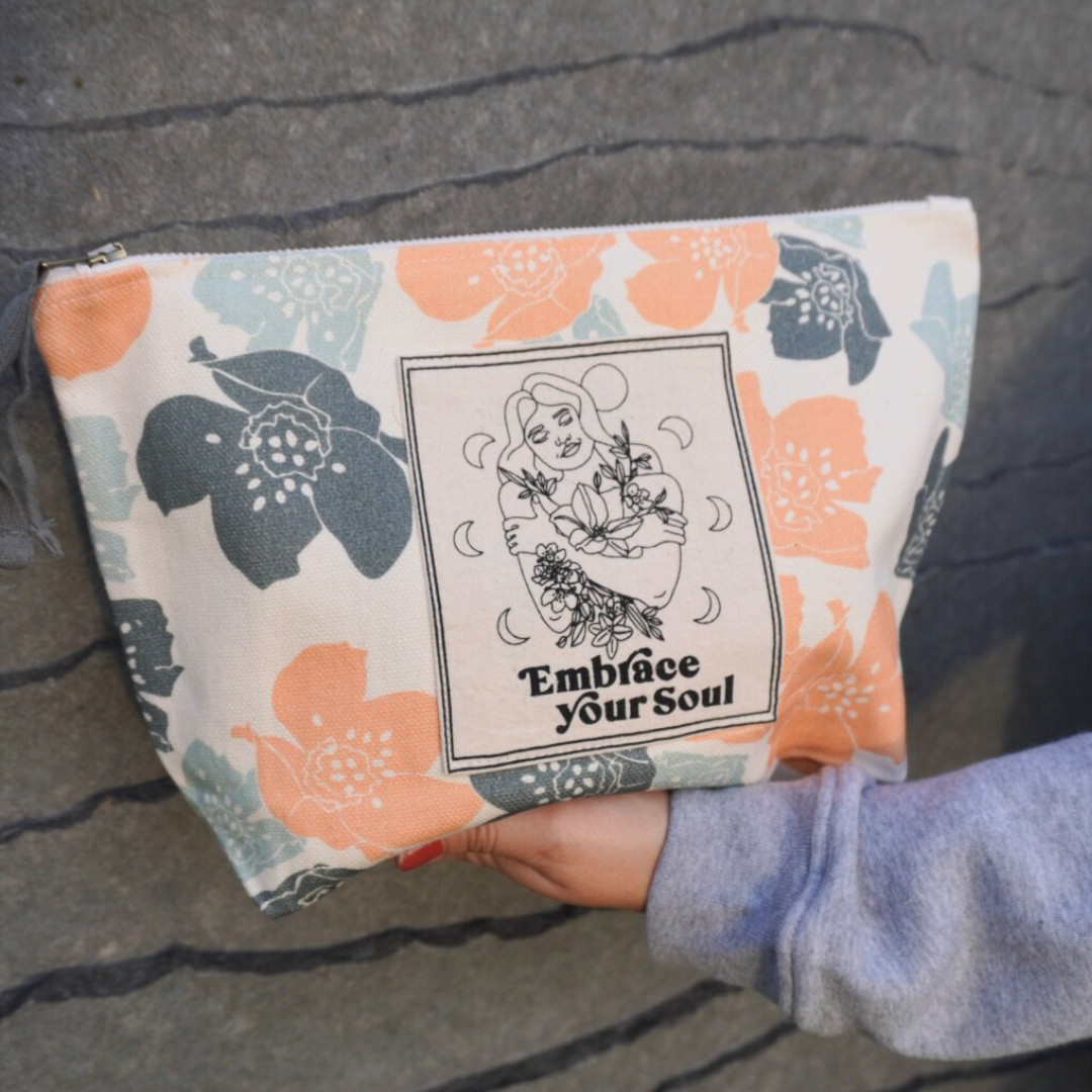 Person hält eine bestickte Tasche mit bunten Blumen und der Aufschrift "Embrace Your Soul" in der Hand.