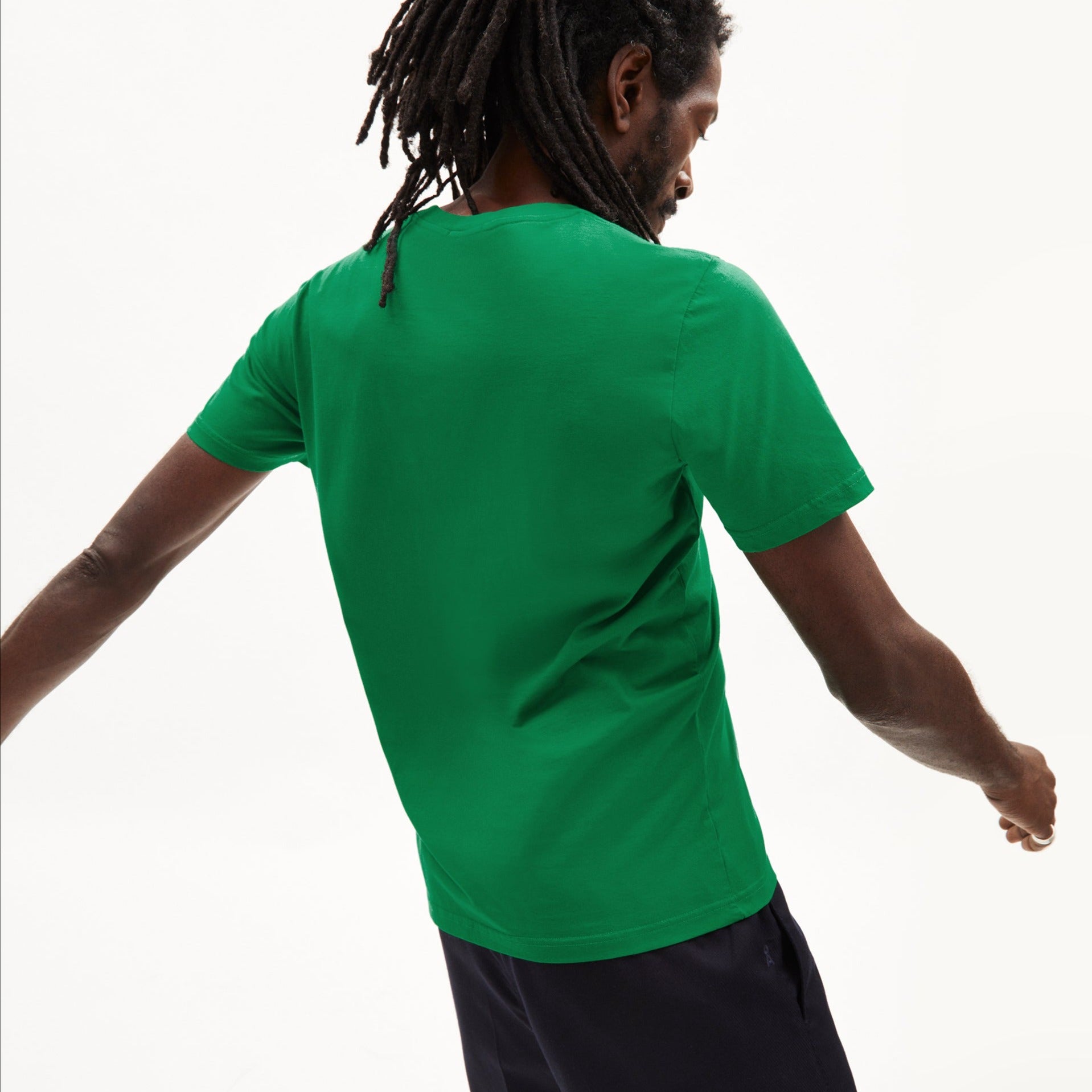Person mit Dreadlocks trägt ein grünes T-Shirt und dreht sich zur Seite vor einem weißen Hintergrund.