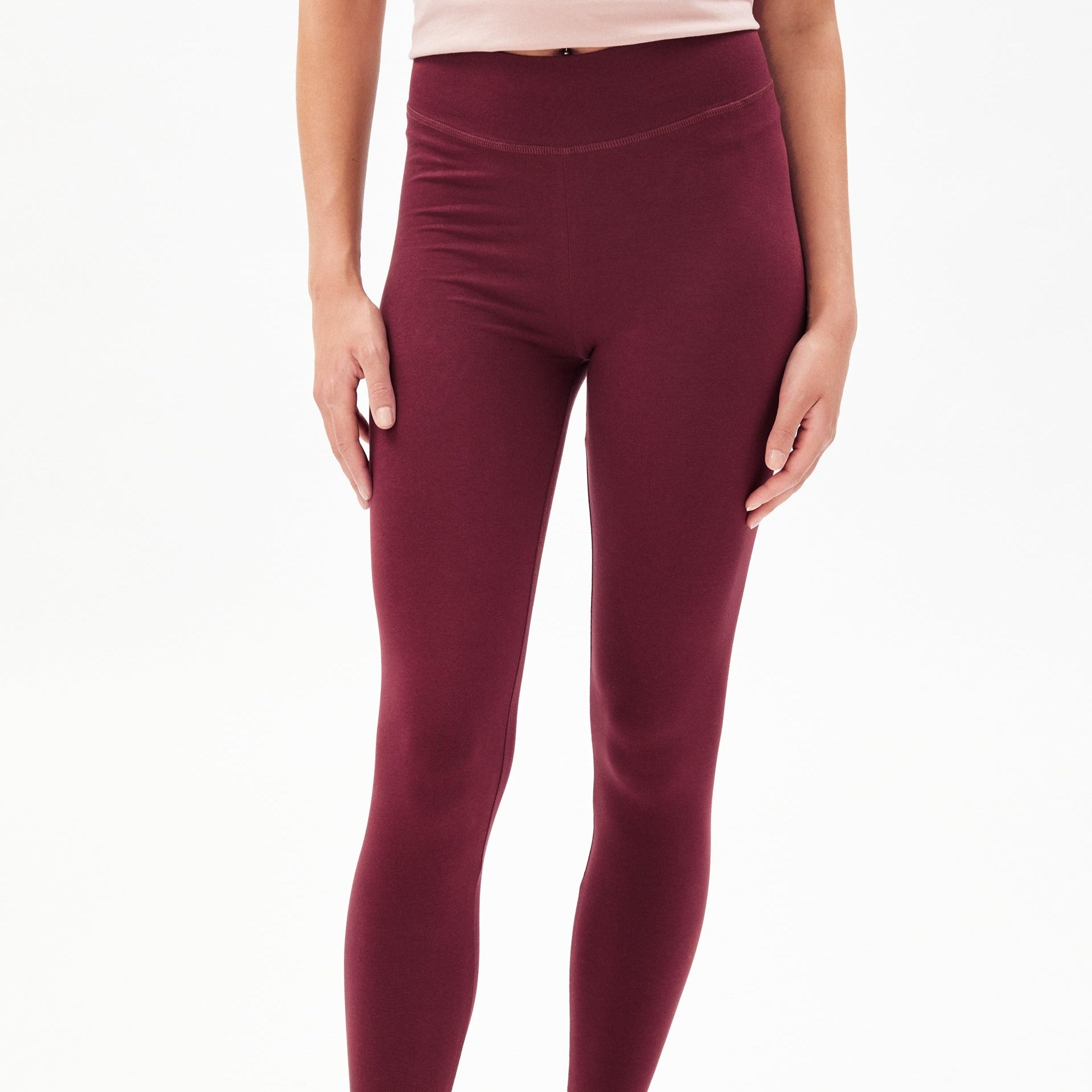 Eine Person trägt weinrote Leggings und ein beigefarbenes Oberteil.