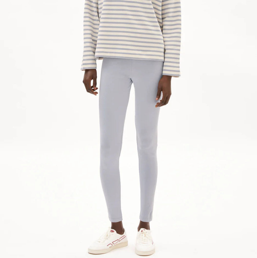 Eine Person, die ein langärmeliges, grau-weiß gestreiftes Hemd, hellgraue Leggings und weiße Turnschuhe trägt, steht vor einem schlichten weißen Hintergrund. Ihr Kopf ist auf dem Bild nicht zu sehen.