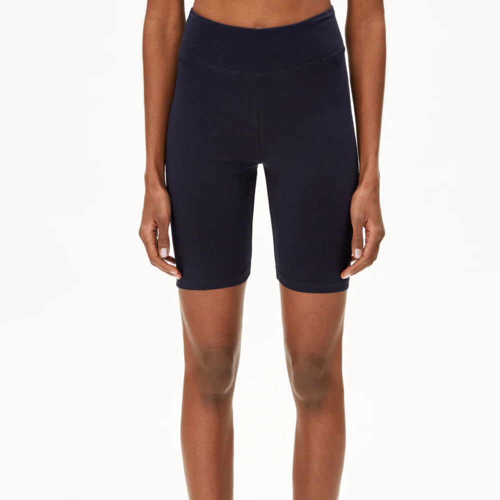 Eine Person, die eine marineblaue Radlerhose mit hoher Taille trägt, steht vor einem einfarbig weißen Hintergrund, die Arme locker an der Seite.