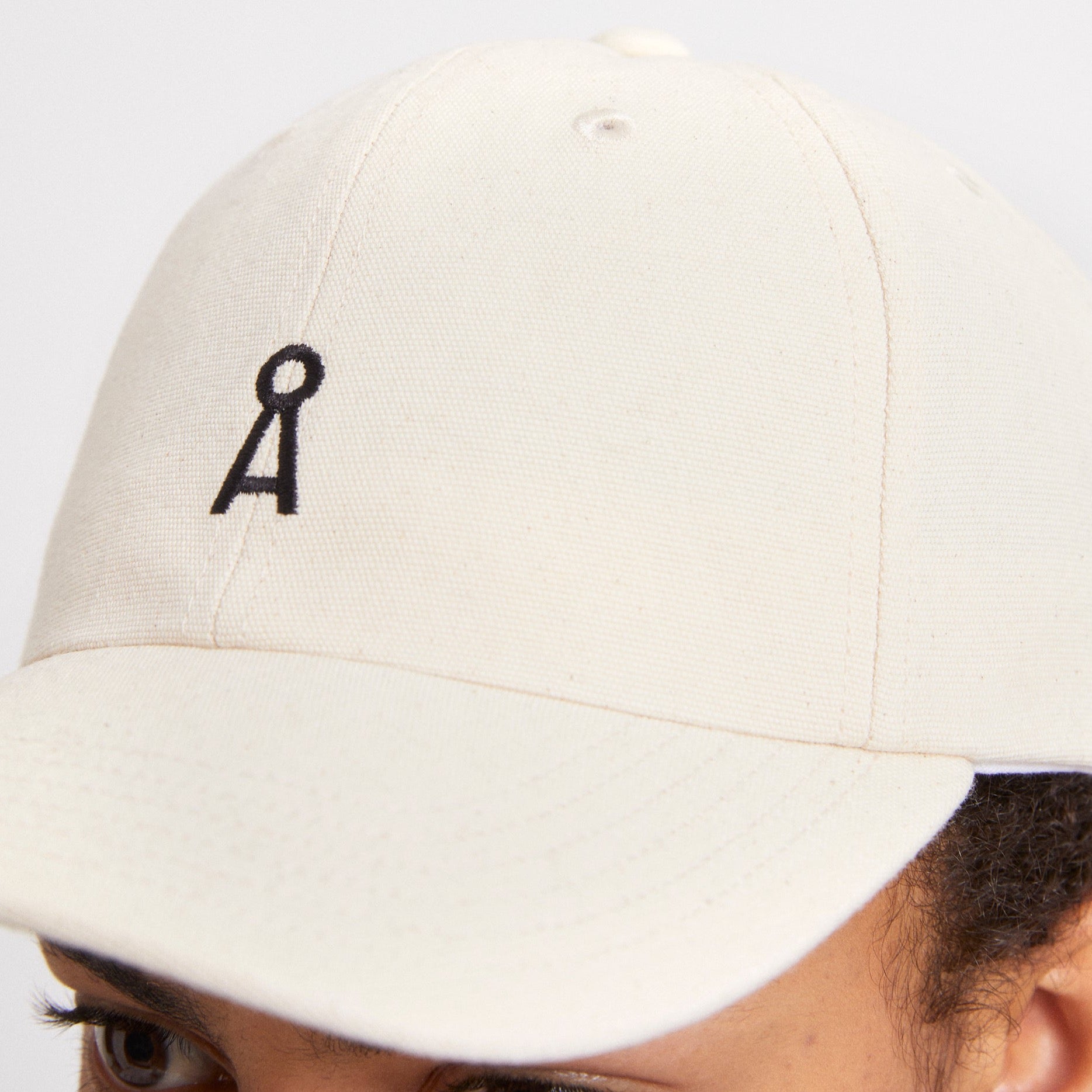 Nahaufnahme einer beigen Kappe mit einem schwarzen gestickten Symbol auf der Vorderseite.