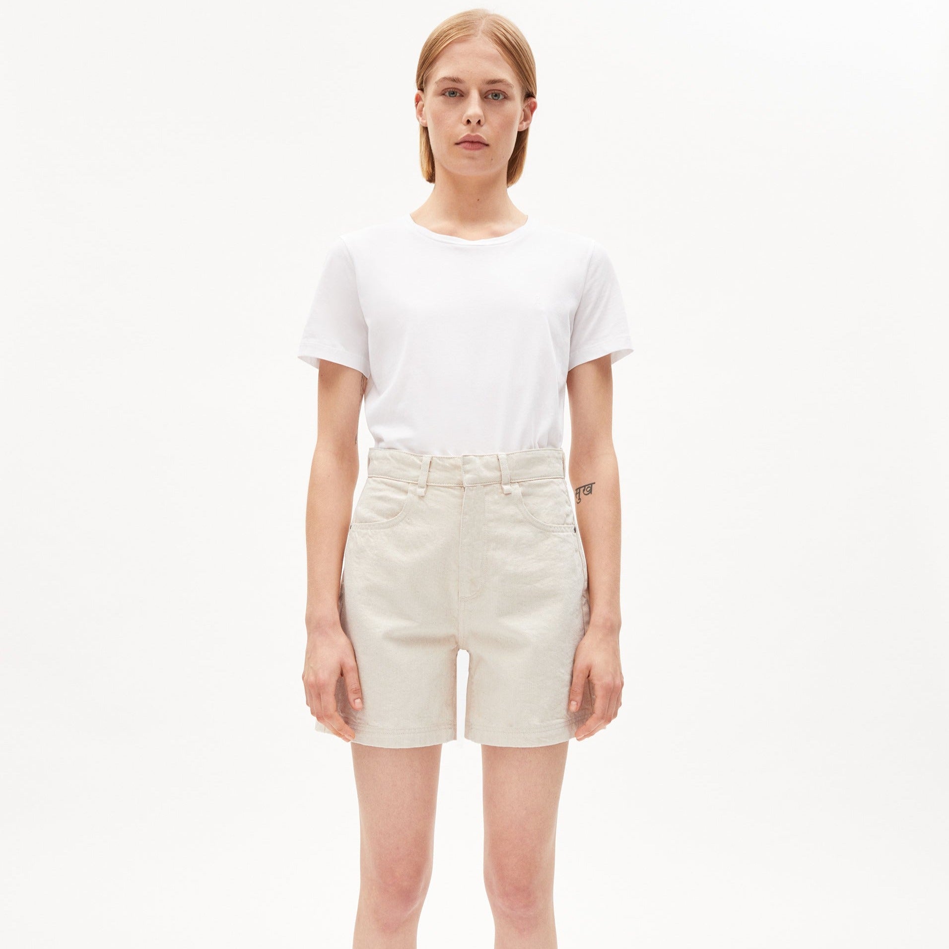 Person in weißem T-Shirt und beigen Shorts steht vor weißem Hintergrund.