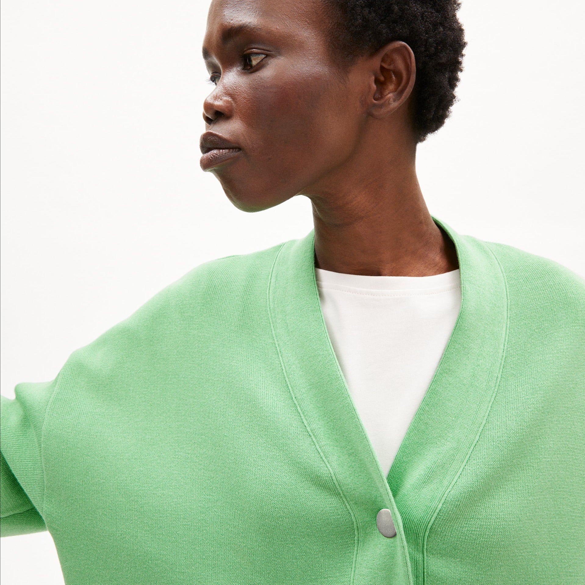 Person in a green cardigan and white shirt looking to the side against a plain background.