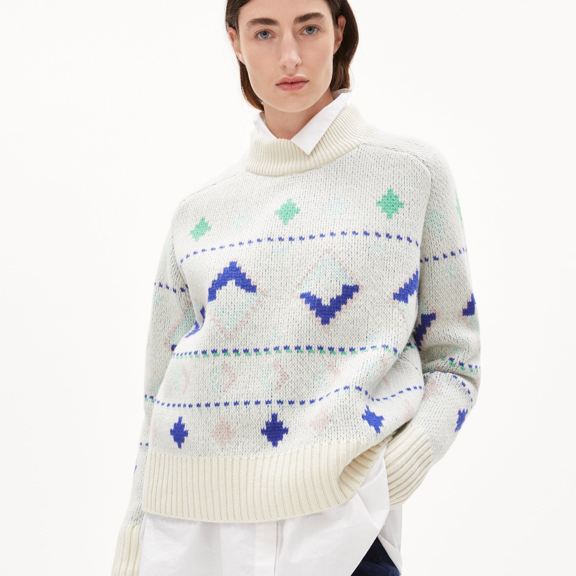 Frau in gemustertem Strickpullover mit Rollkragen und über weißem Hemd.