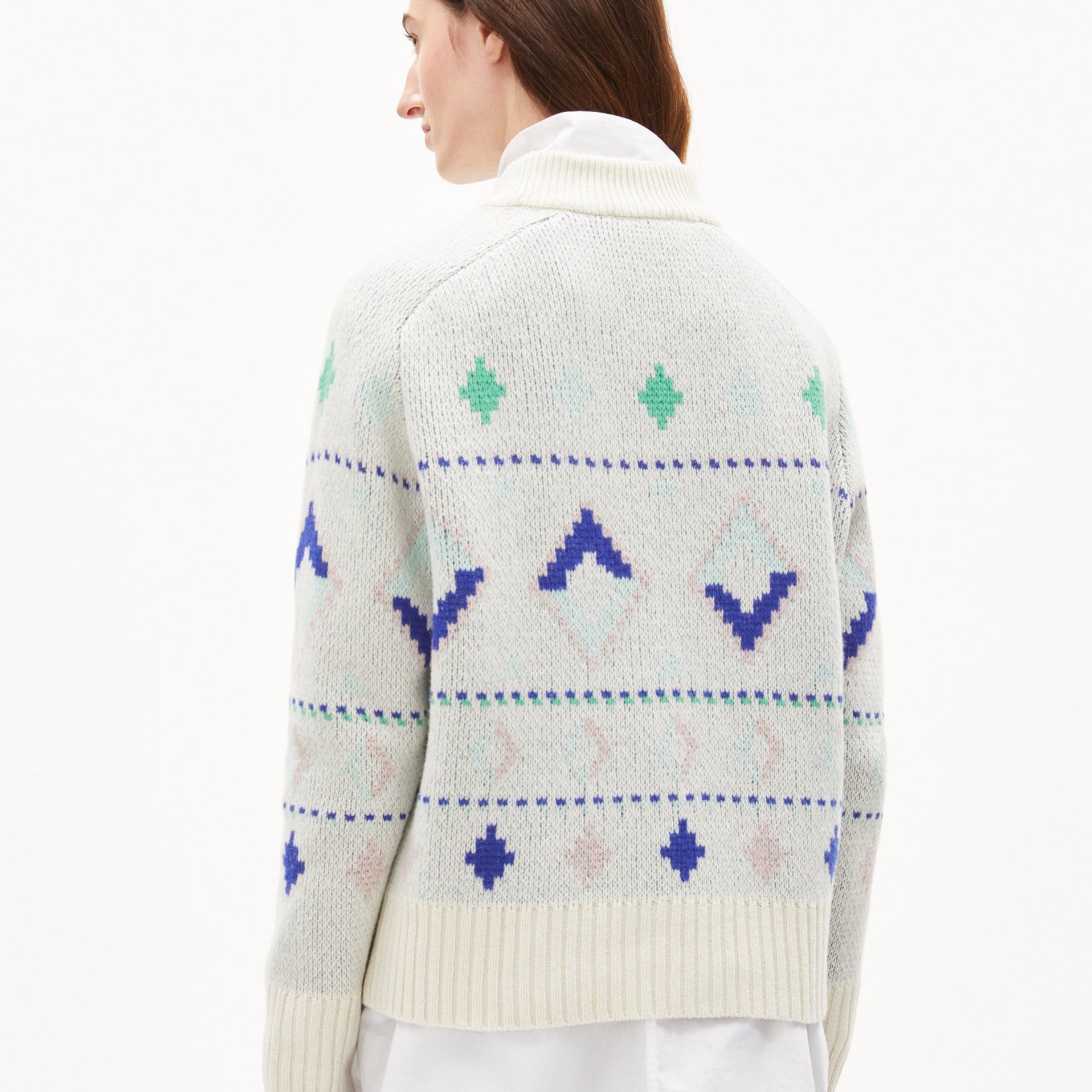 Frau trägt einen cremefarbenen Pullover mit blau-grünem geometrischem Muster und hohem Kragen, von hinten gesehen.