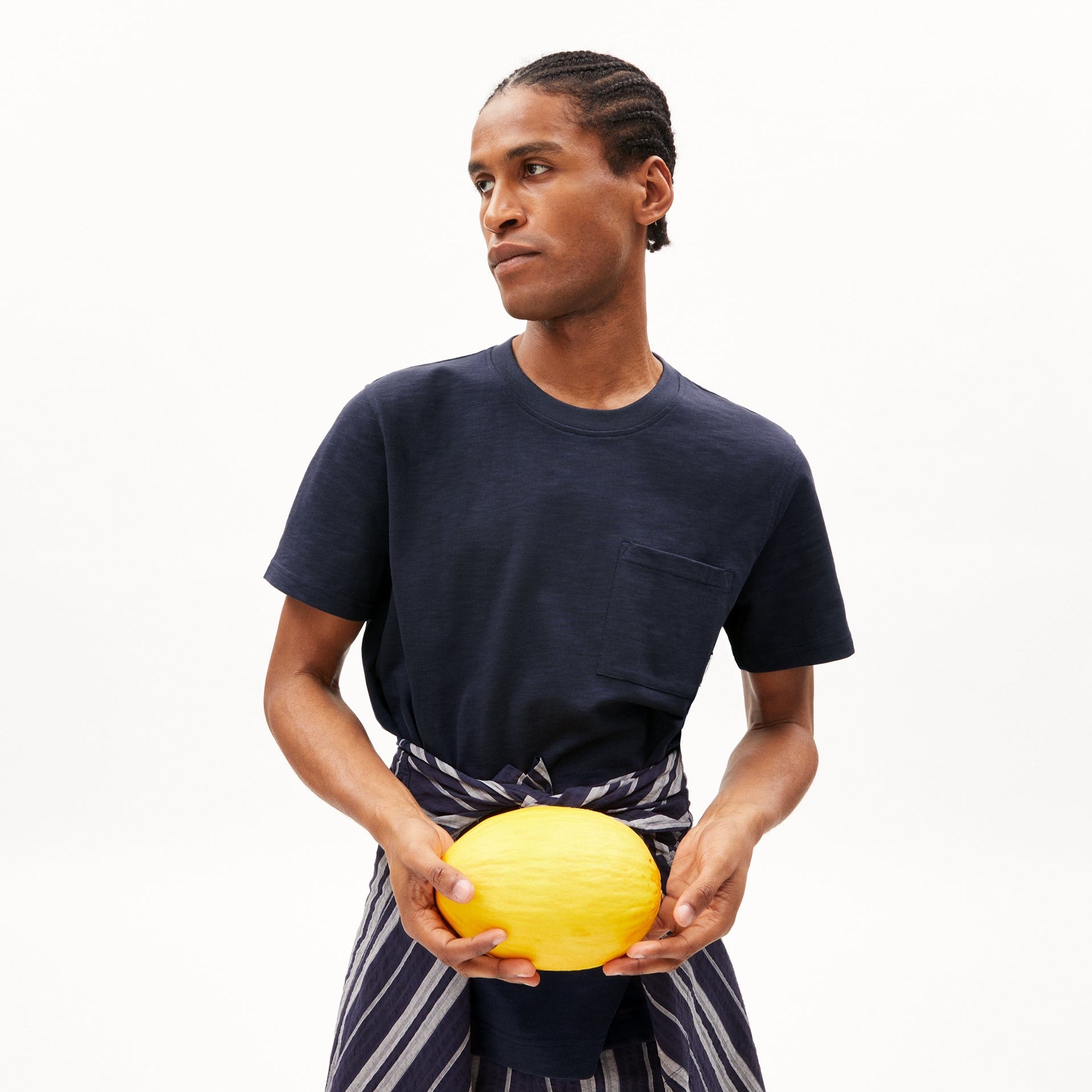 Ein Mann in einem dunkelblauen T-Shirt hält eine gelbe Melone, ein gestreiftes Tuch um die Hüften gebunden.