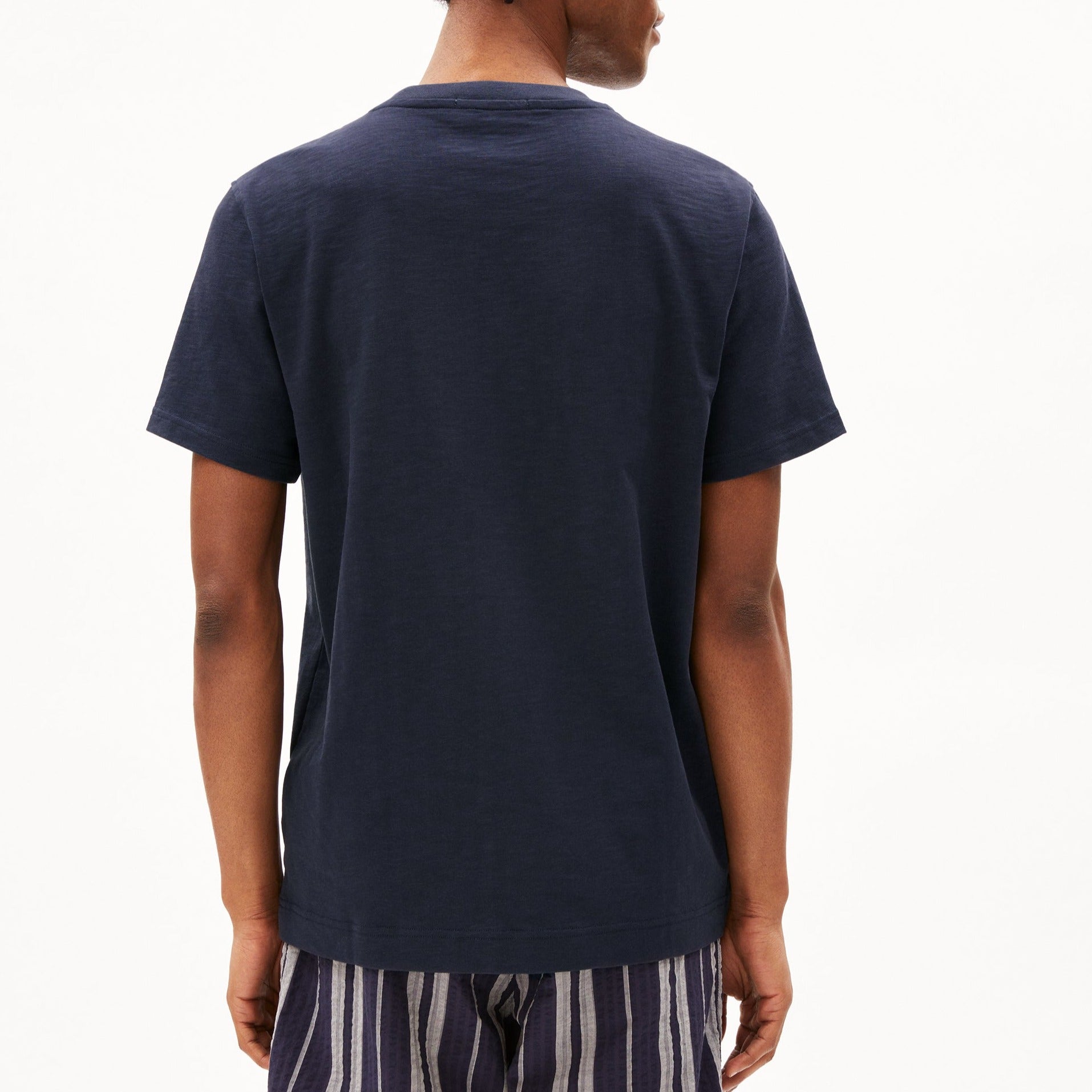 Person in navy T-shirt and striped pants, viewed from the back against a plain white background.