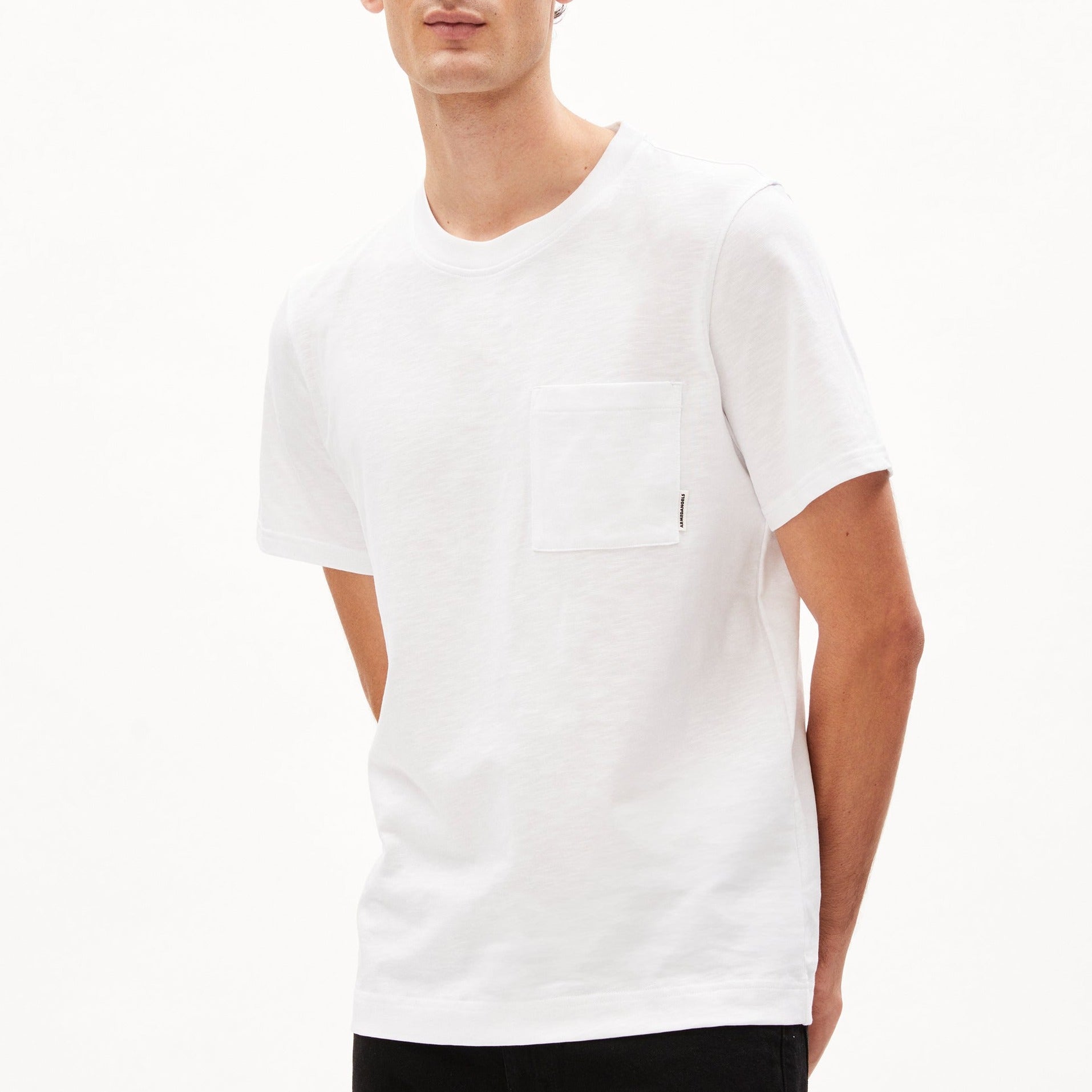 Eine Person trägt ein schlichtes weißes T-Shirt mit Brusttasche vor einem weißen Hintergrund.