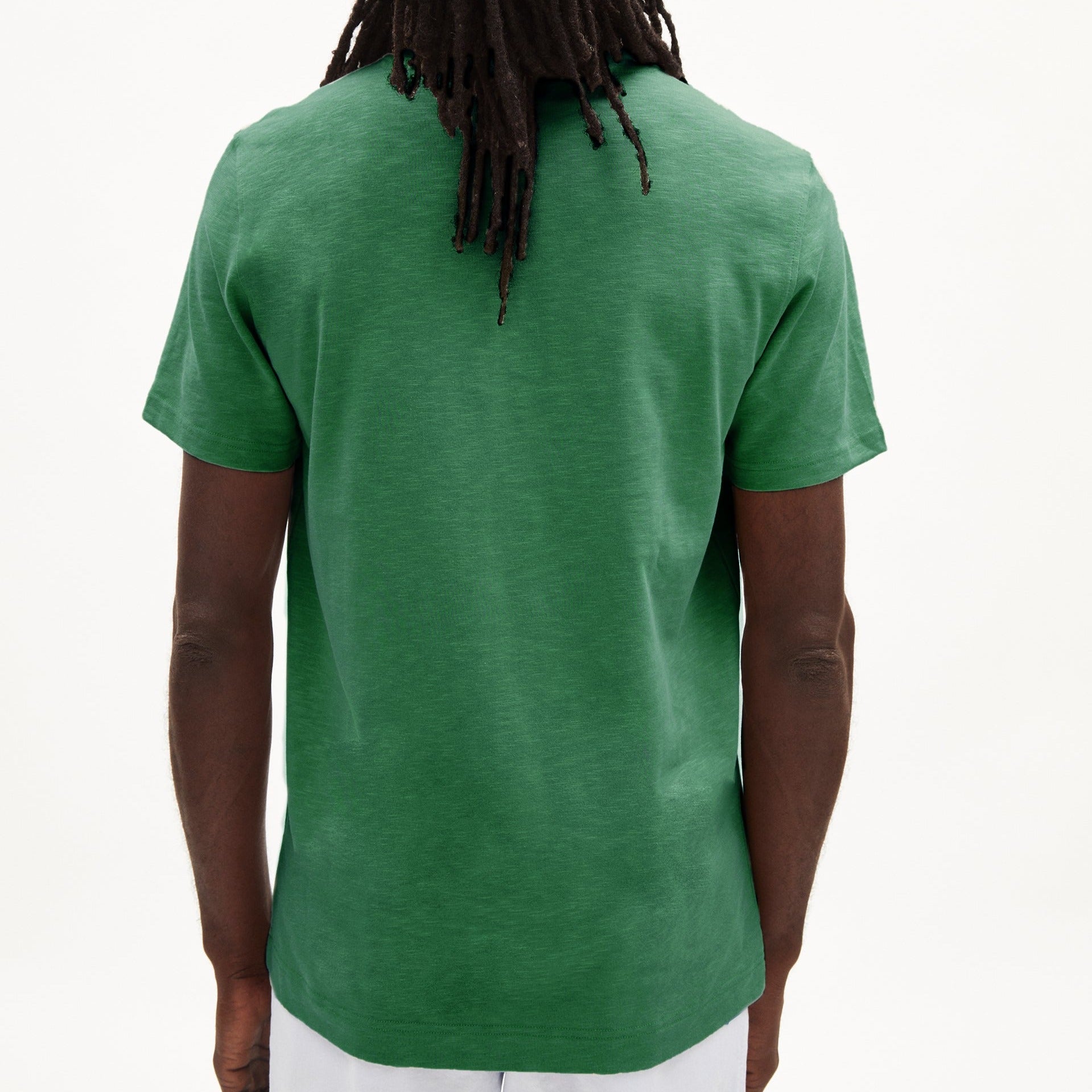 Eine Person trägt ein grünes T-Shirt, von hinten fotografiert, mit langen Haaren, vor weißem Hintergrund.