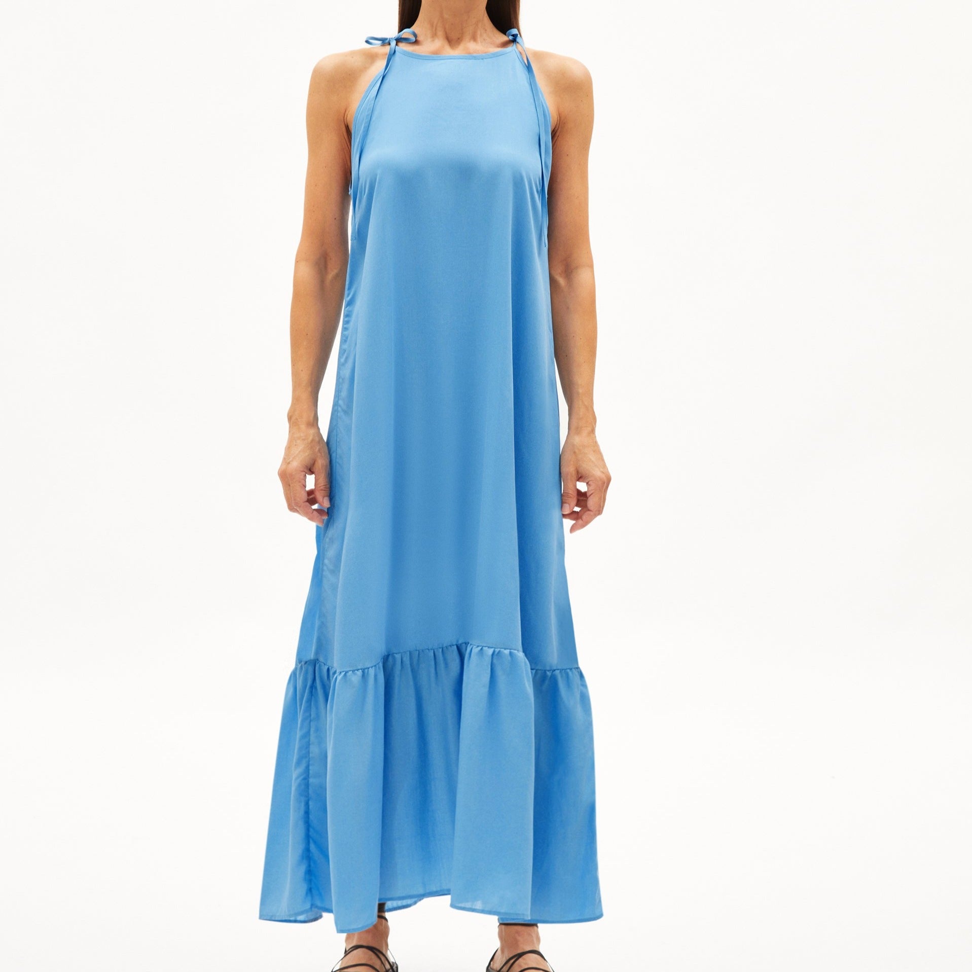 Person in einem langen blauen Neckholder-Kleid mit Rüschen am Saum, stehend auf weißem Hintergrund.