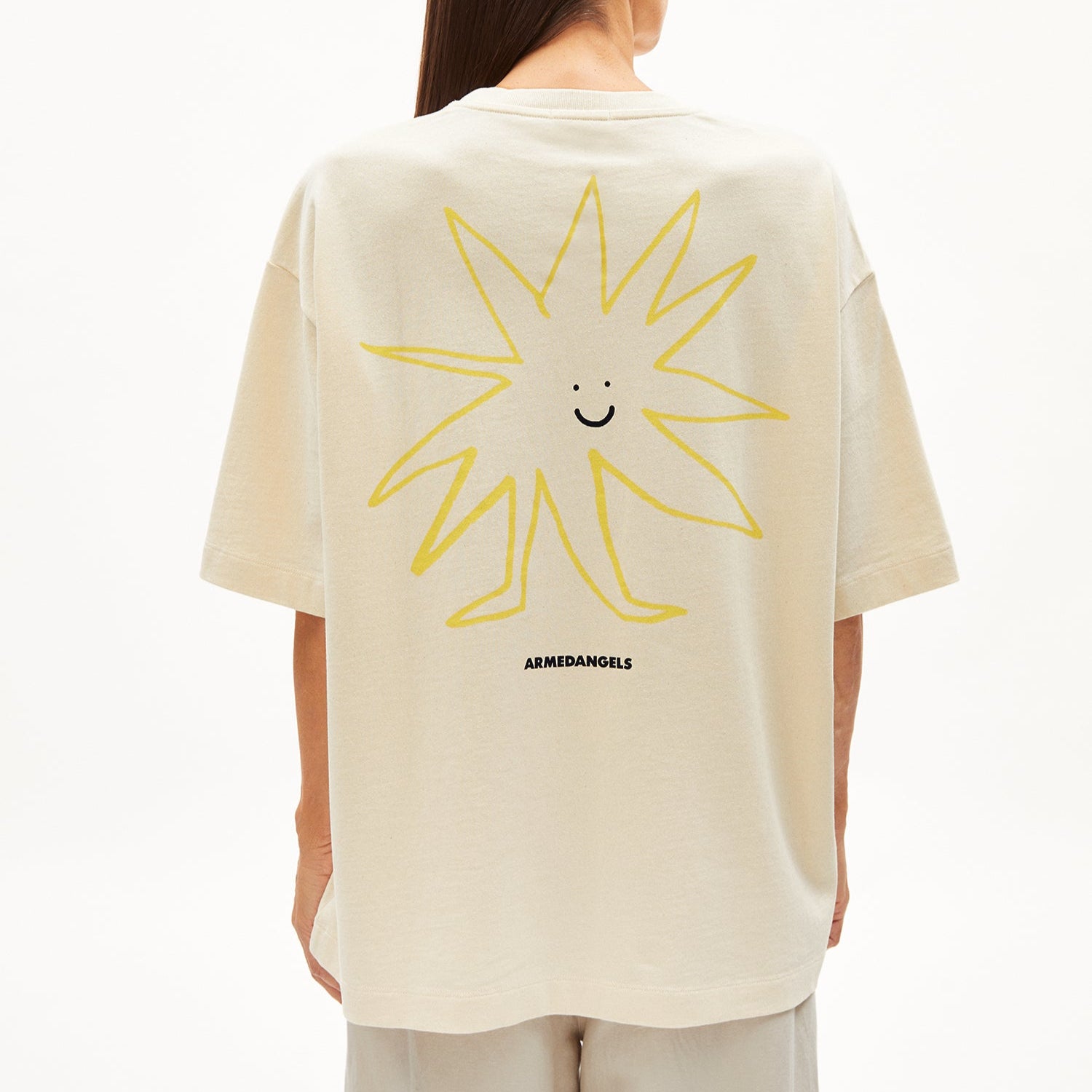 Person mit beigem T-Shirt mit gelbem, lächelndem Sonnenmotiv auf dem Rücken und der Aufschrift "ARMEDANGELS".