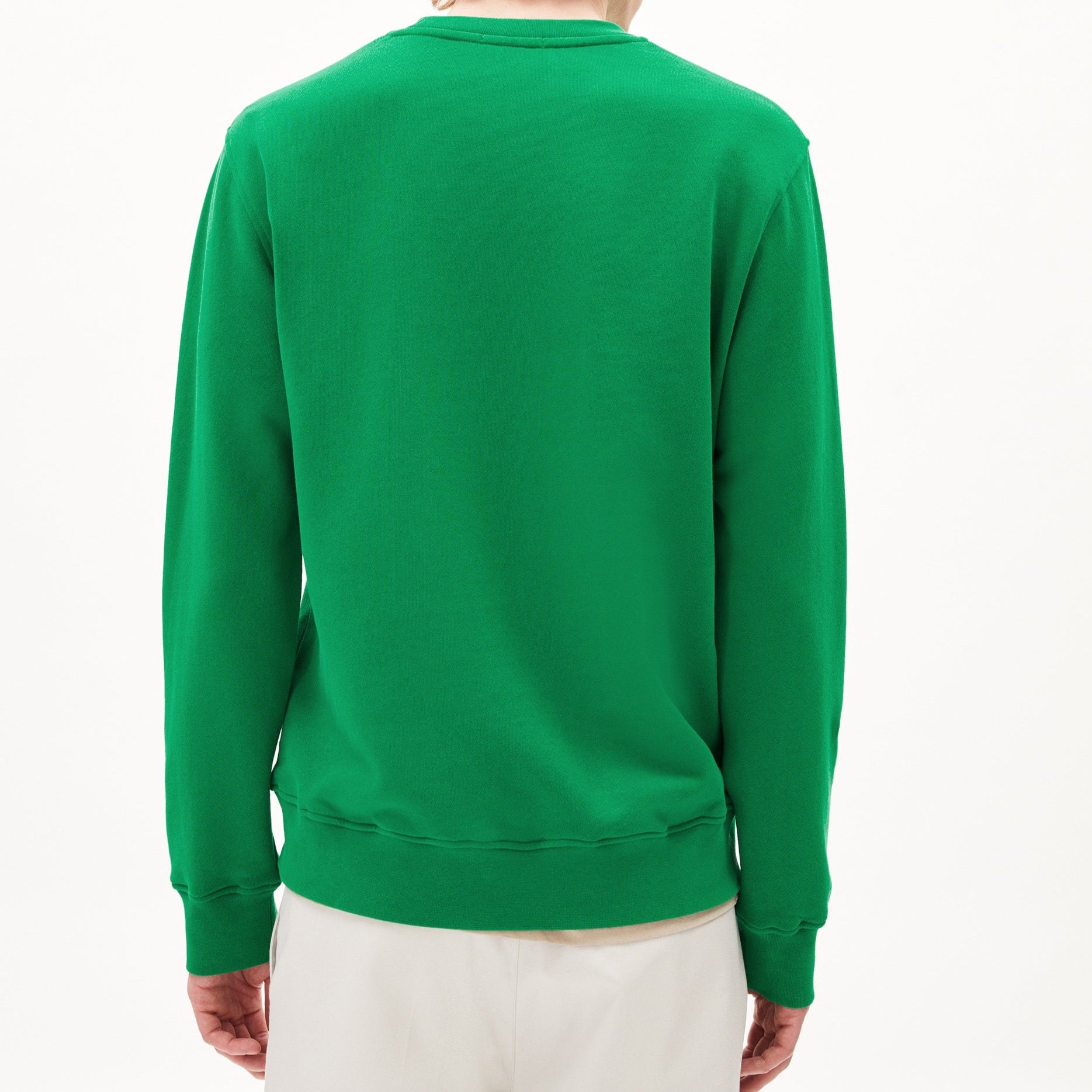 Eine Person trägt einen grünen Pullover und weiße Hosen, mit dem Rücken zur Kamera gewandt.