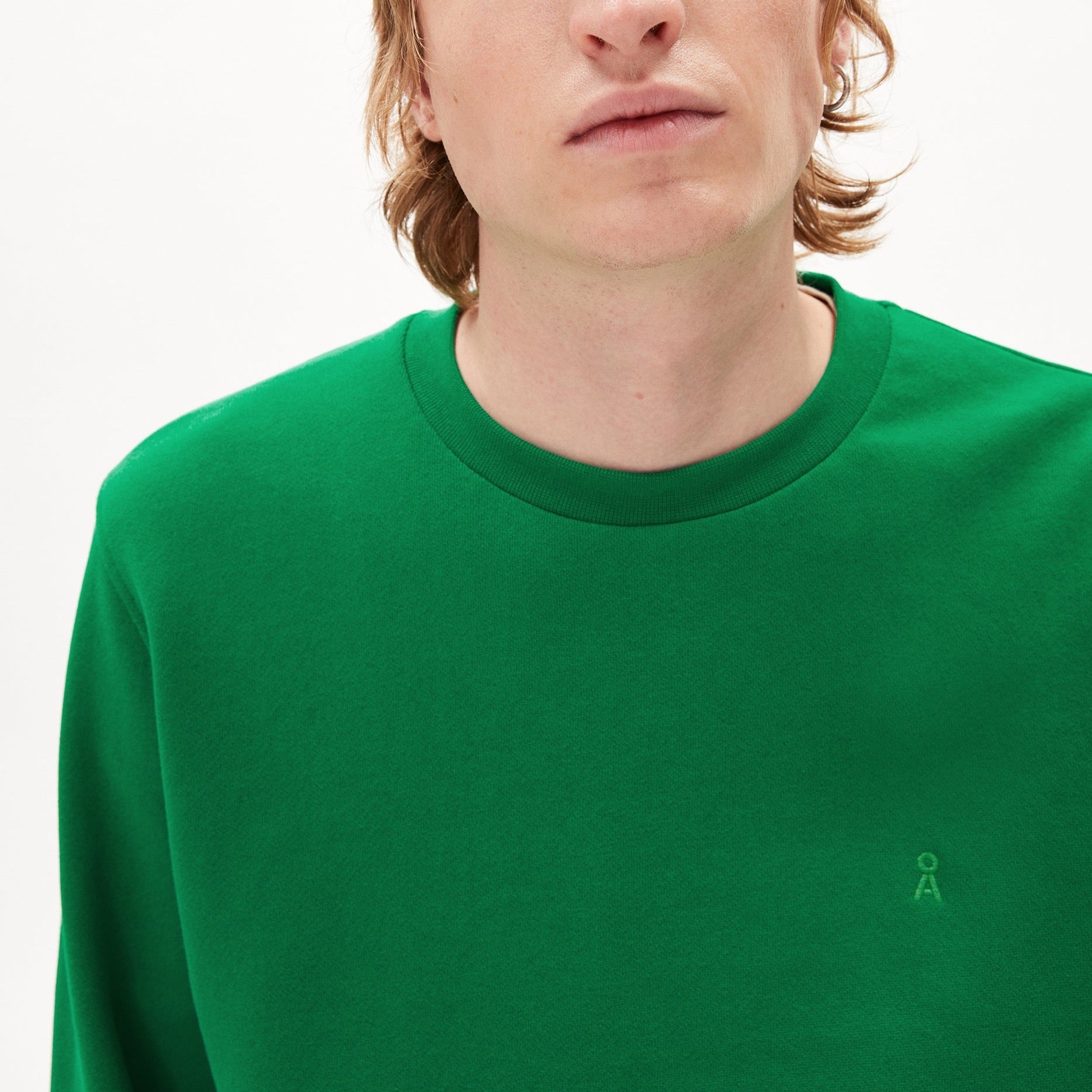 Person in a green sweatshirt with a small logo on the chest against a plain white background.