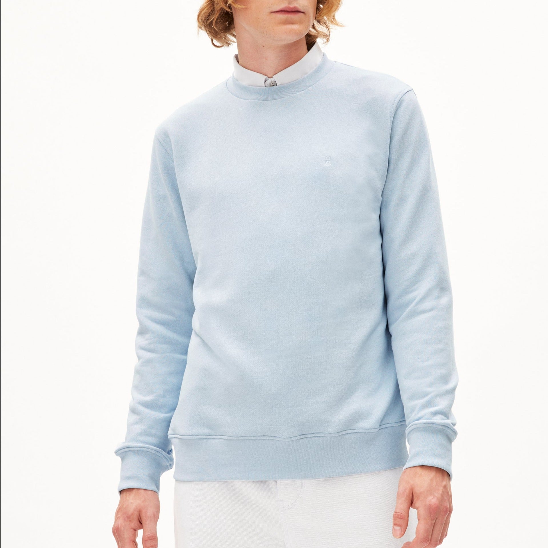 Person in einem hellblauen Pullover und weißem Hemd vor neutralem Hintergrund.