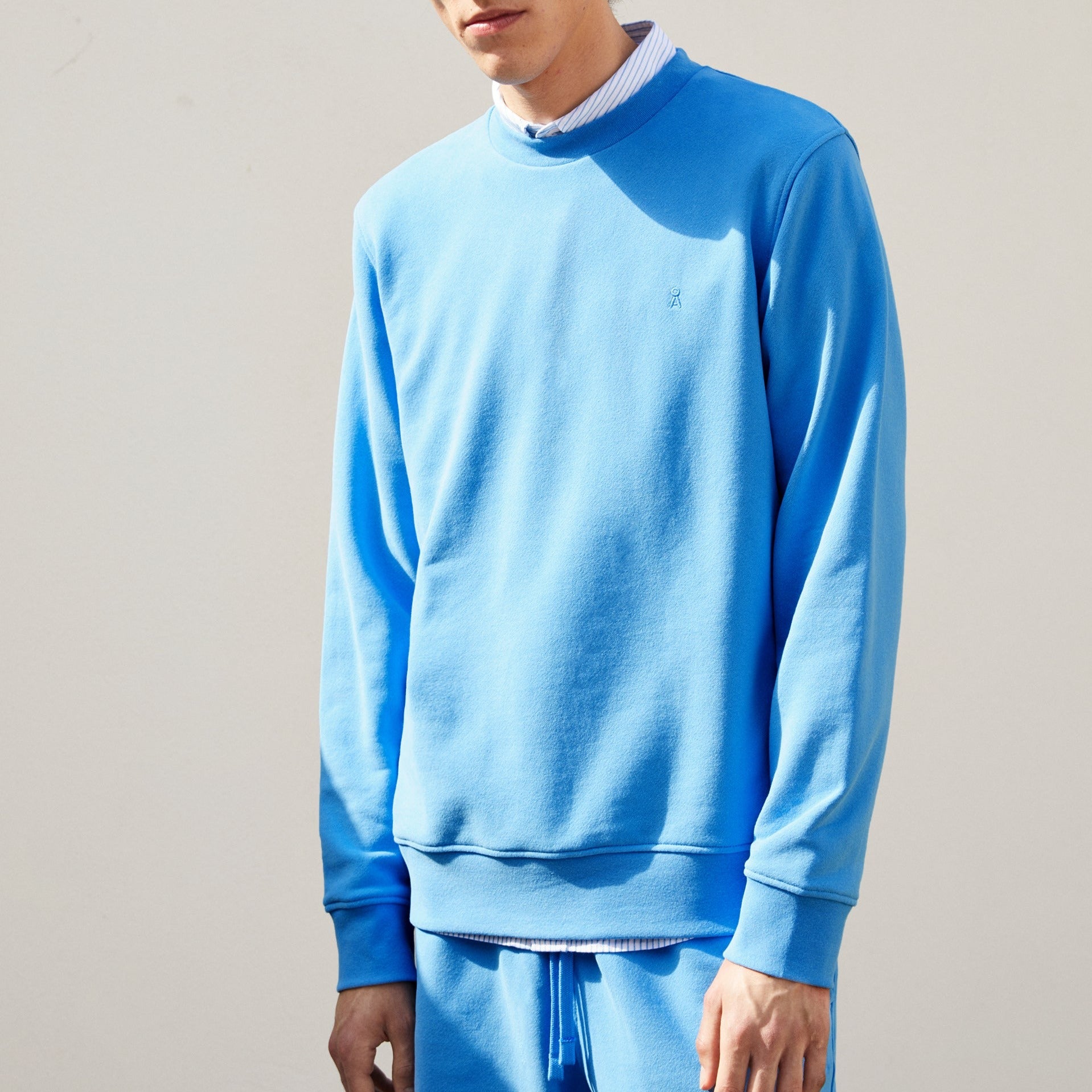 Person in blauem Pullover und passender Jogginghose, vor einem neutralen Hintergrund stehend.