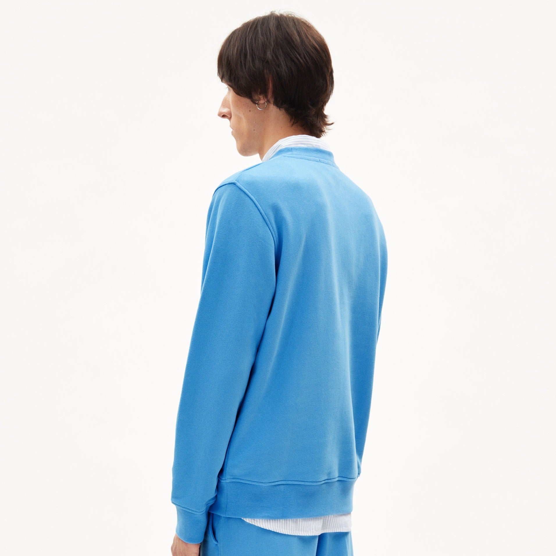 Person in blauer Sportkleidung steht mit dem Rücken zur Kamera vor einem weißen Hintergrund.