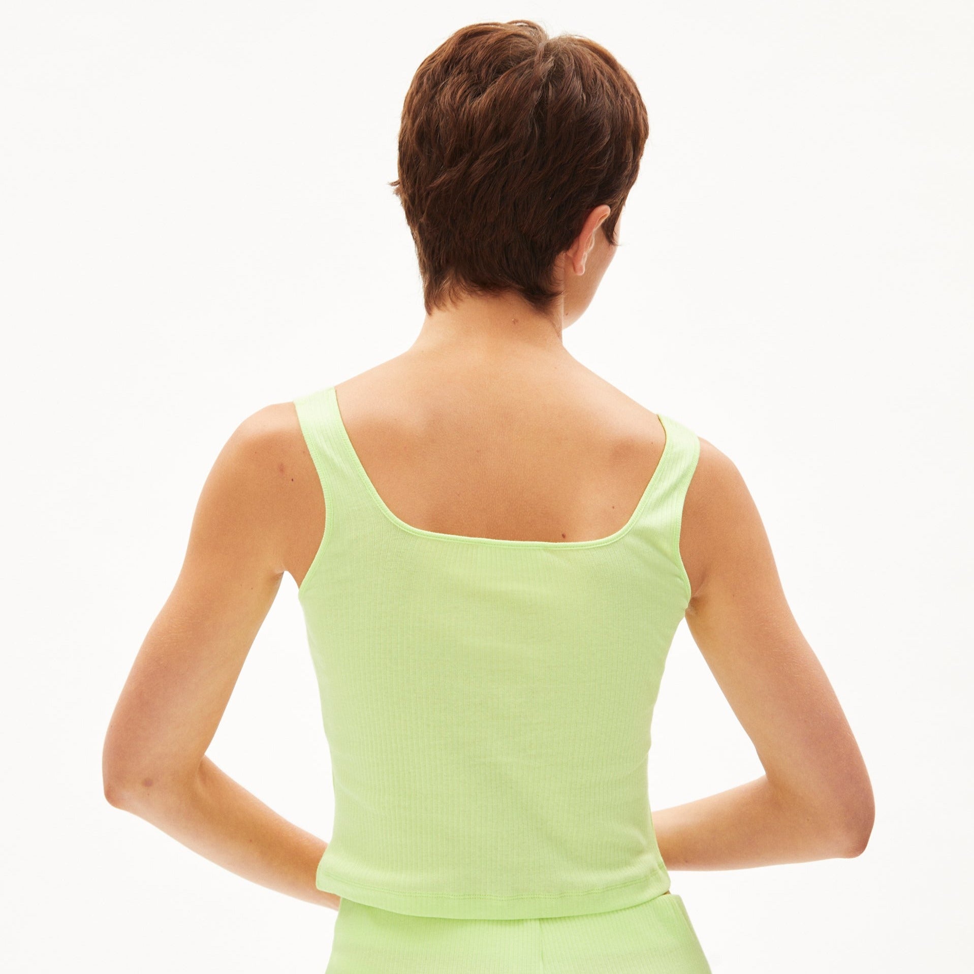 Person in lime green tank top and matching bottoms, viewed from the back, with short brown hair, on a plain white background.