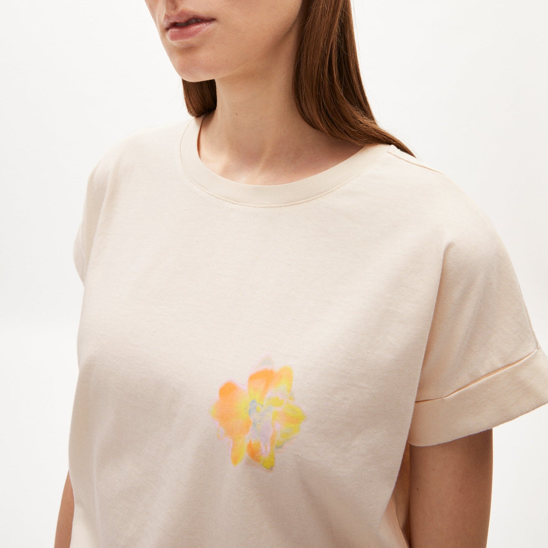 Frau in hellem T-Shirt mit aufgedrucktem, buntem Blumenmotiv vor weißem Hintergrund.
