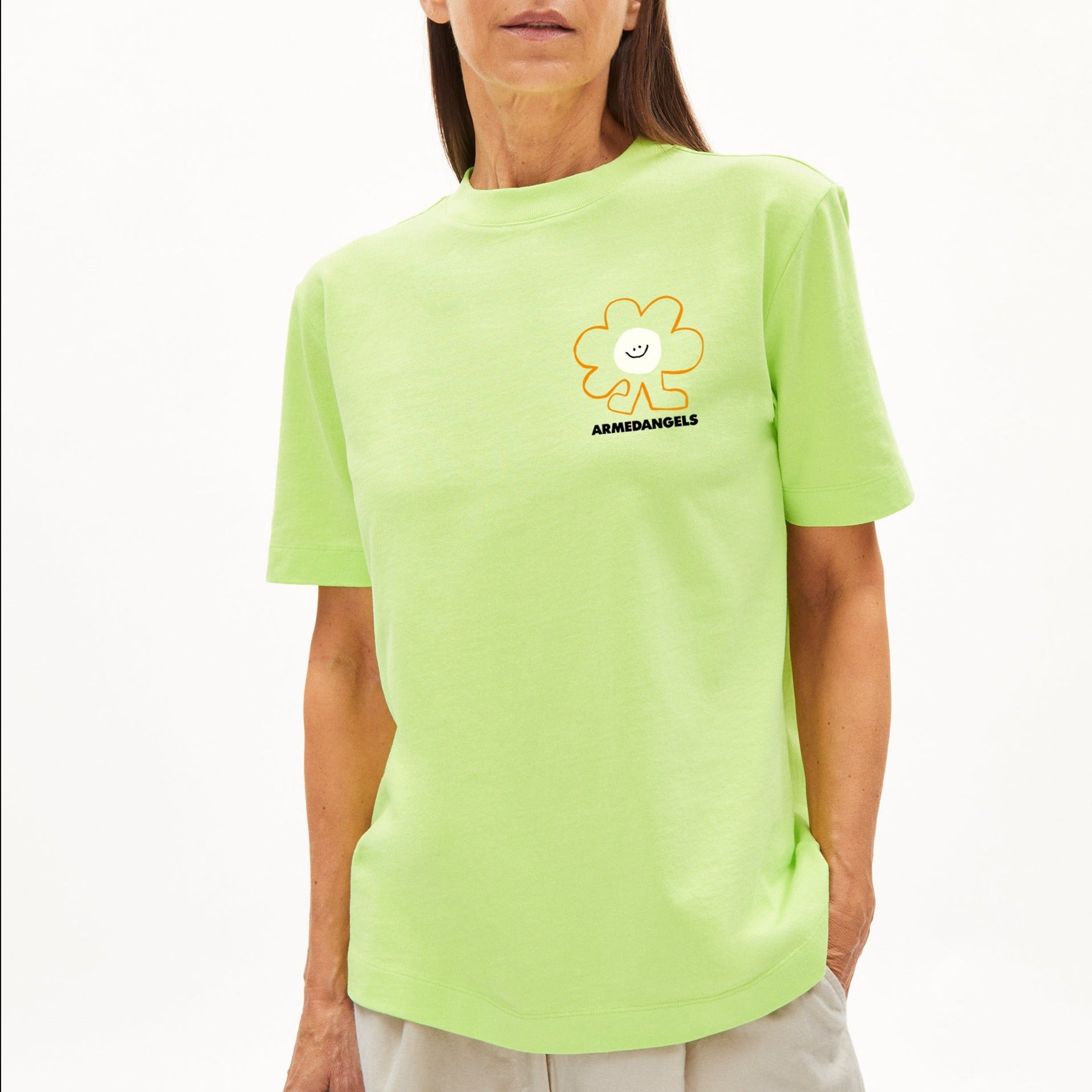 Frau trägt ein neongrünes T-Shirt mit einem lächelnden Blumen-Logo und dem Schriftzug "Armedangels" auf der Brust.