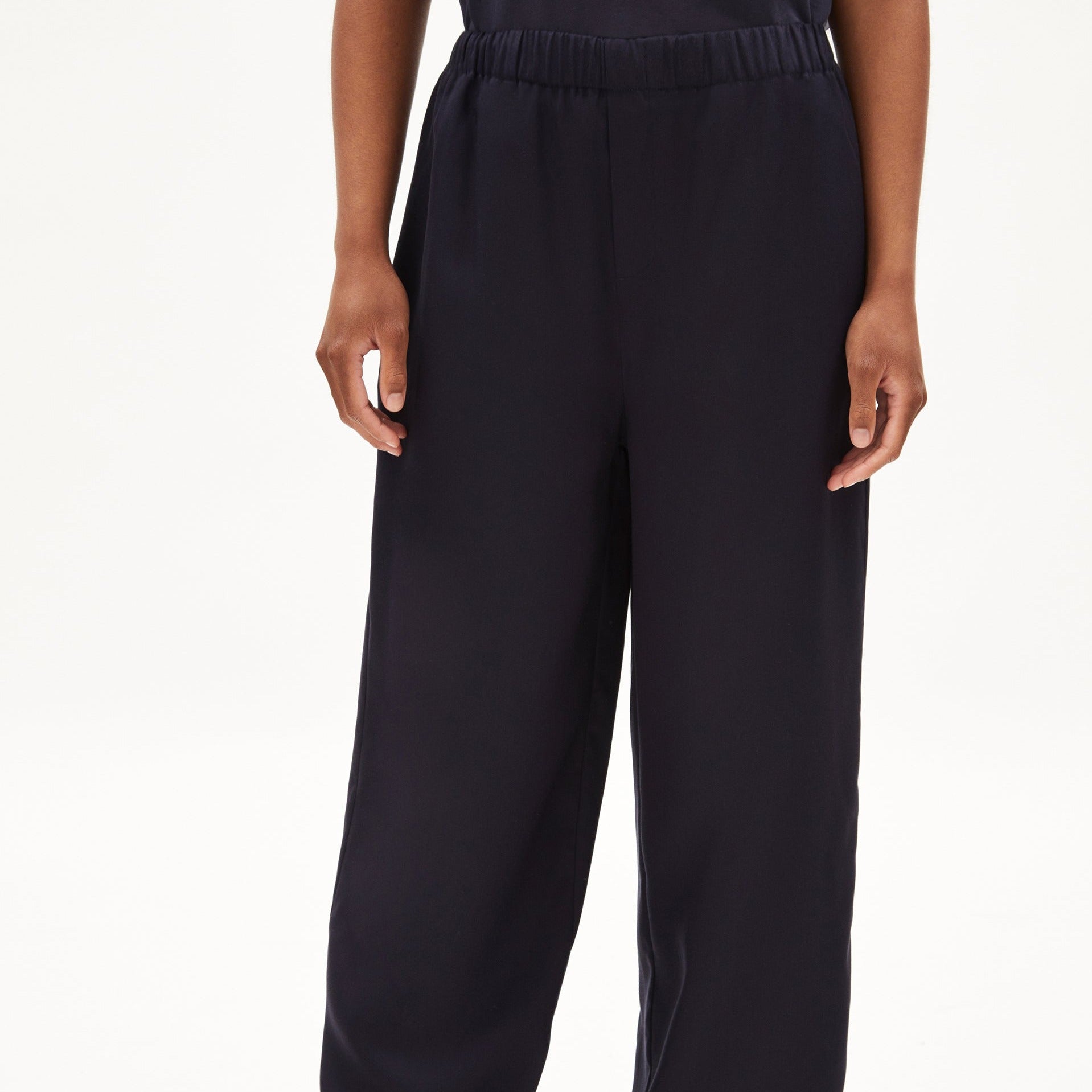 Person trägt eine dunkelblaue, locker sitzende Hose mit elastischem Bund, die bis zum Boden reicht, vor weißem Hintergrund.