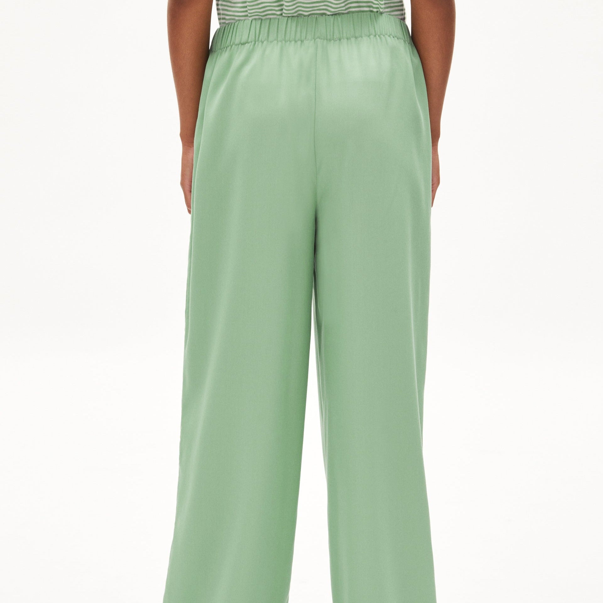 Eine Person trägt eine hellgrüne, weit geschnittene Hose mit elastischem Bund, von hinten fotografiert.