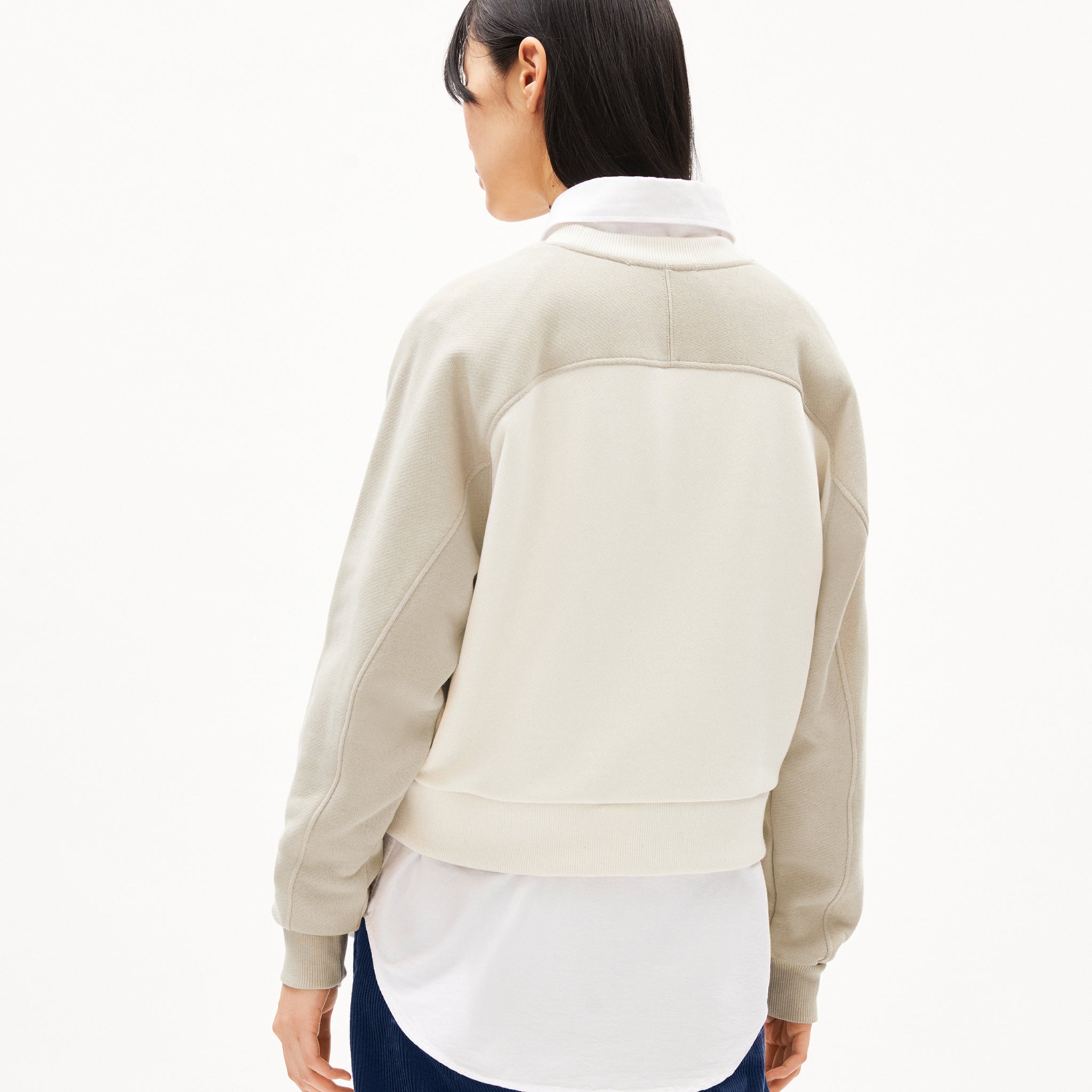 Person von hinten in beigefarbener Jacke und weißem Hemd vor weißem Hintergrund.