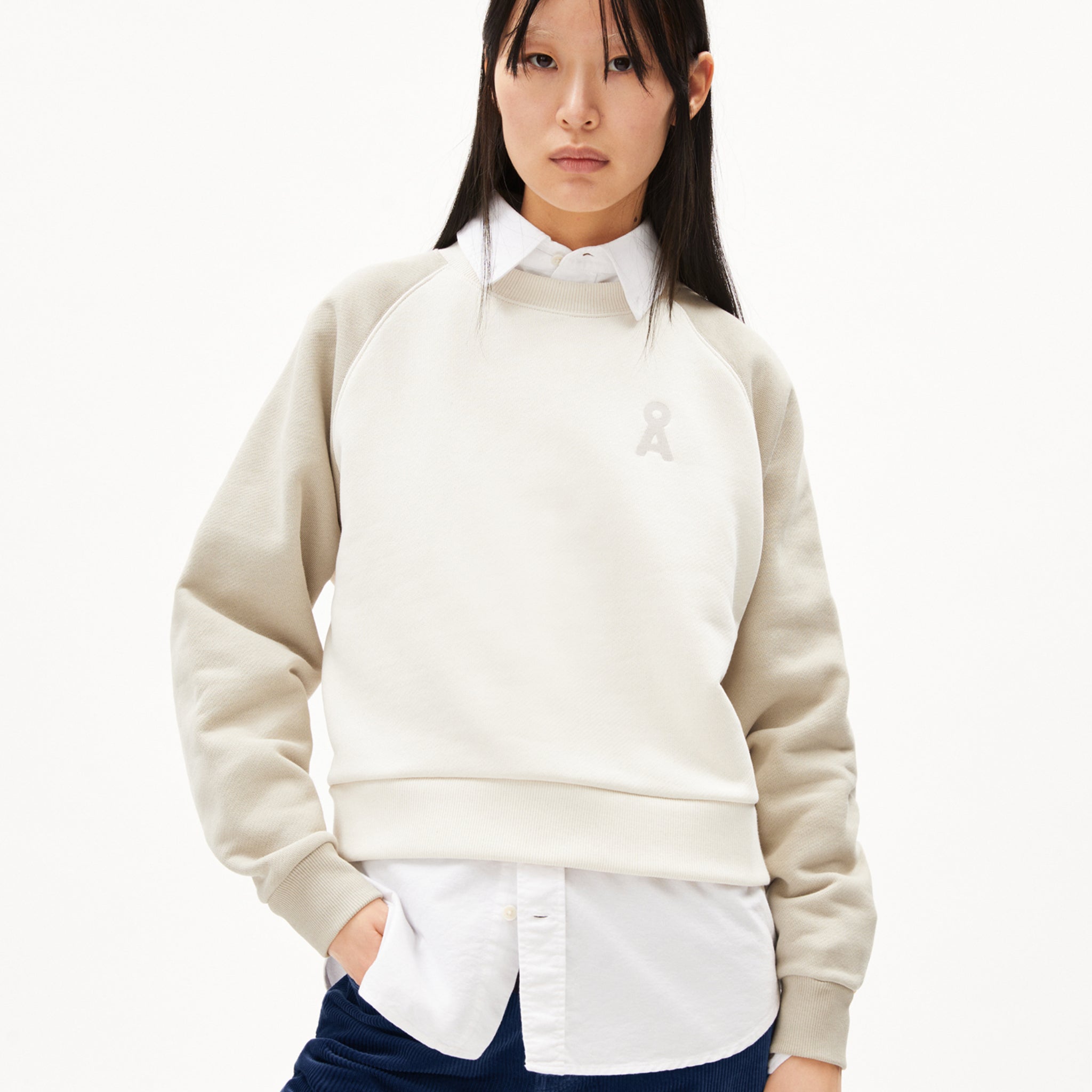 Person in hellbeigem Sweatshirt über einem weißen Hemd vor weißem Hintergrund.