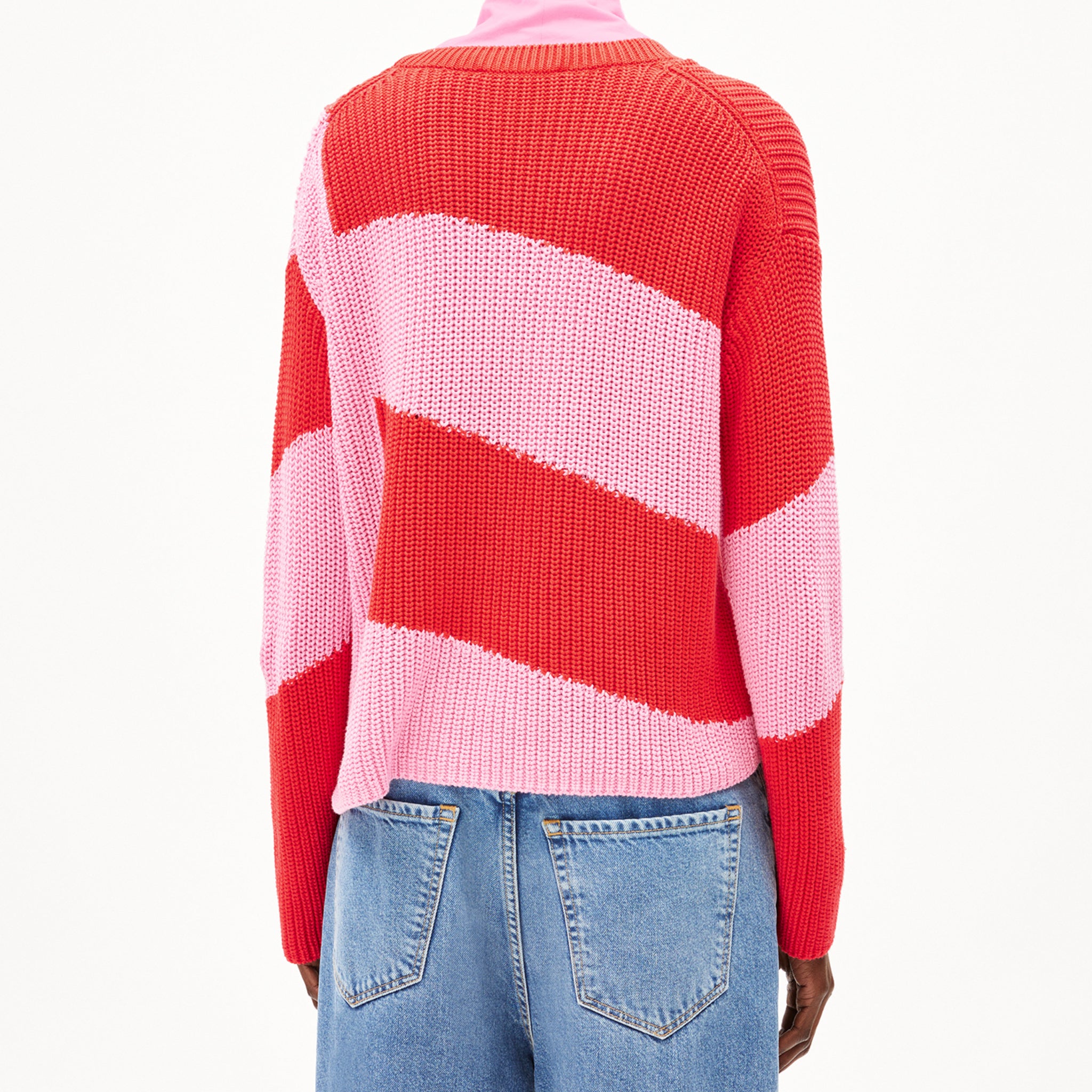 Person trägt einen rot-rosa gestreiften Pullover und blaue Jeans, von hinten gesehen.