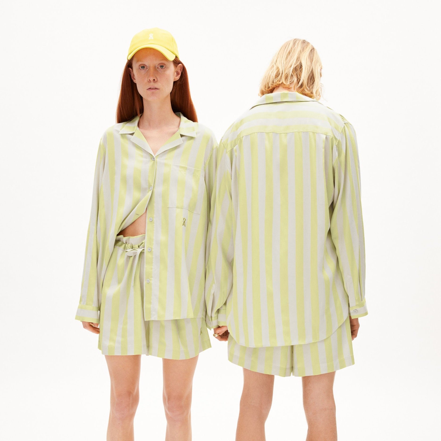 Zwei Personen in gestreiften gelb-weißen Outfits; eine trägt eine Baseballkappe, die andere ist vom Rücken zu sehen.