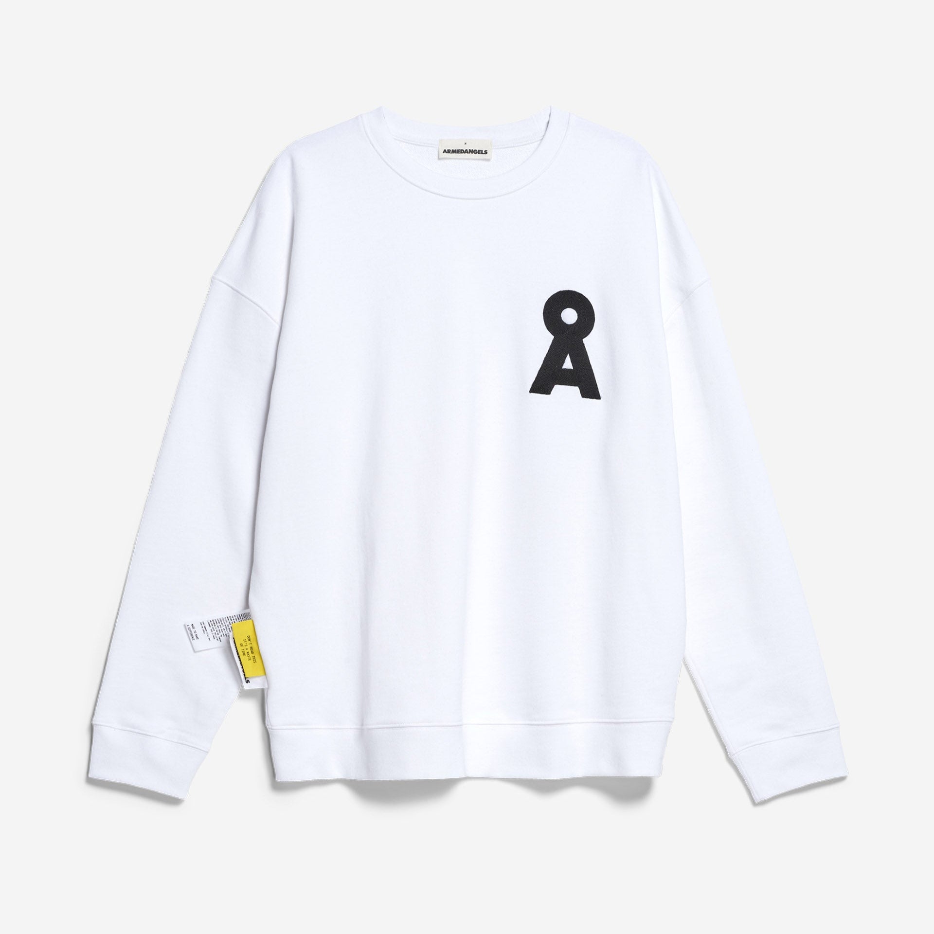 Ein schlichtes weißes Sweatshirt mit einem schwarzen stilisierten Buchstaben A auf der linken Brust und einem kleinen gelben Etikett, das in der Nähe des unteren Saums auf der rechten Seite angebracht ist, vor einem hellgrauen Hintergrund.