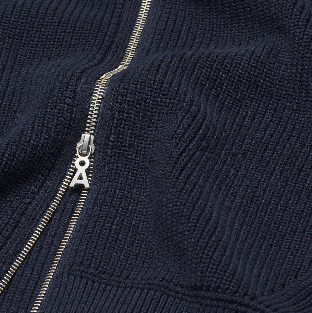 Nahaufnahme eines marineblauen gerippten Stoffes mit einem silbernen Reißverschluss, der teilweise geöffnet ist und die detaillierte Struktur und die Nähte des Materials zeigt.