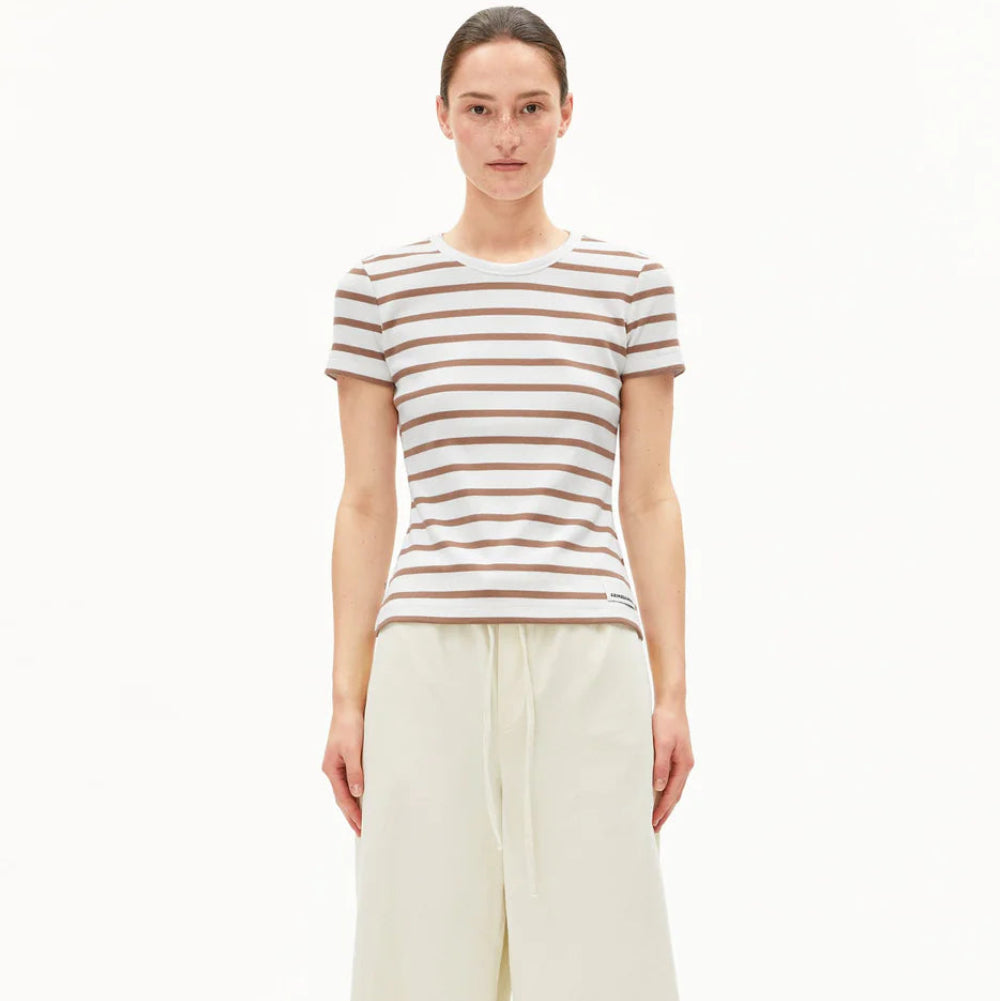 Eine Person steht vor einem weißen Hintergrund und trägt ein kurzärmeliges, beige-weiß gestreiftes T-Shirt und eine cremefarbene Hose mit weitem Bein und hoher Taille, an deren unterem Ende weiße Schuhe zu sehen sind.