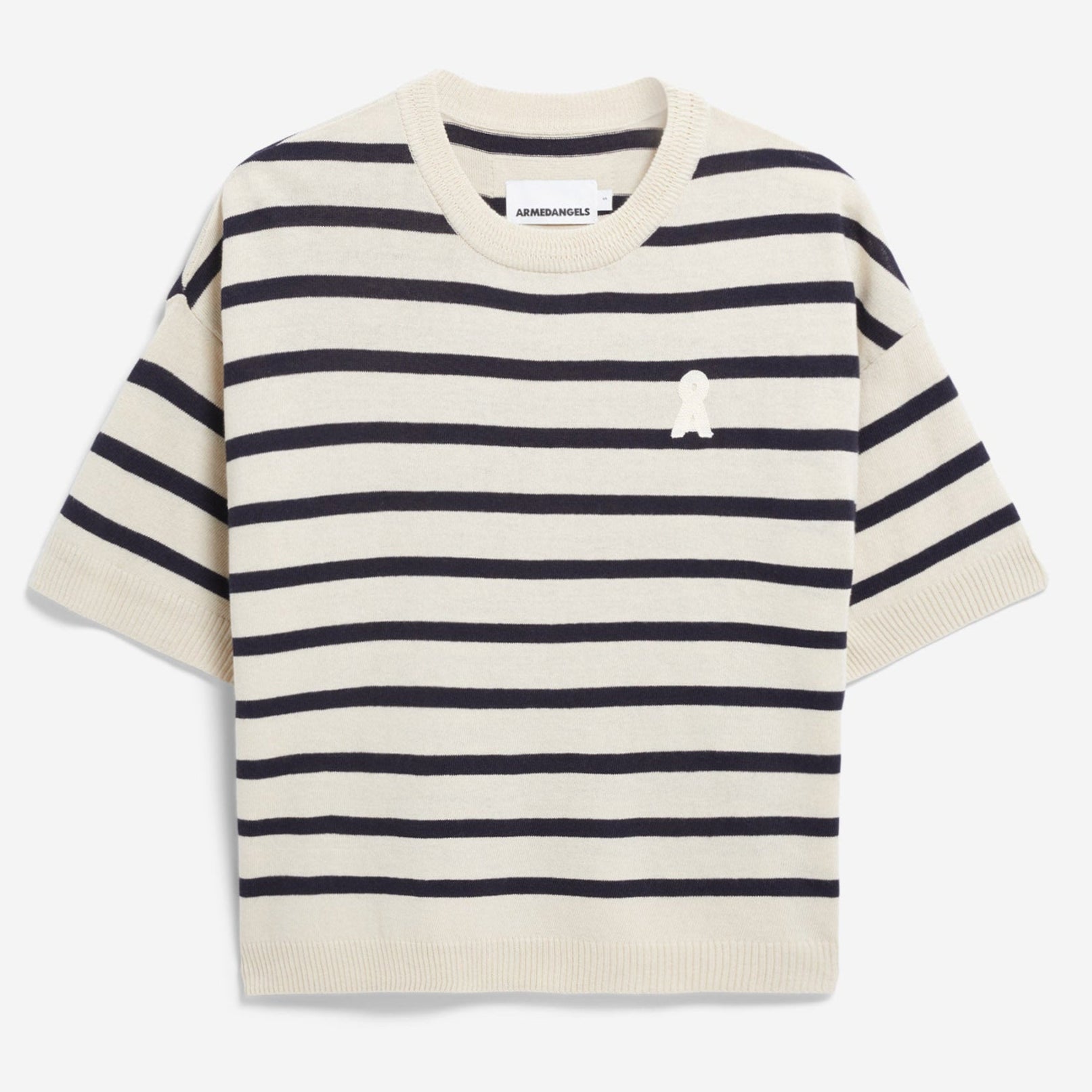 Ein cremefarbener kurzärmeliger Pullover mit horizontalen schwarzen Streifen und einem kleinen weißen gestickten Aufnäher auf der linken Brust, flach auf weißem Grund.