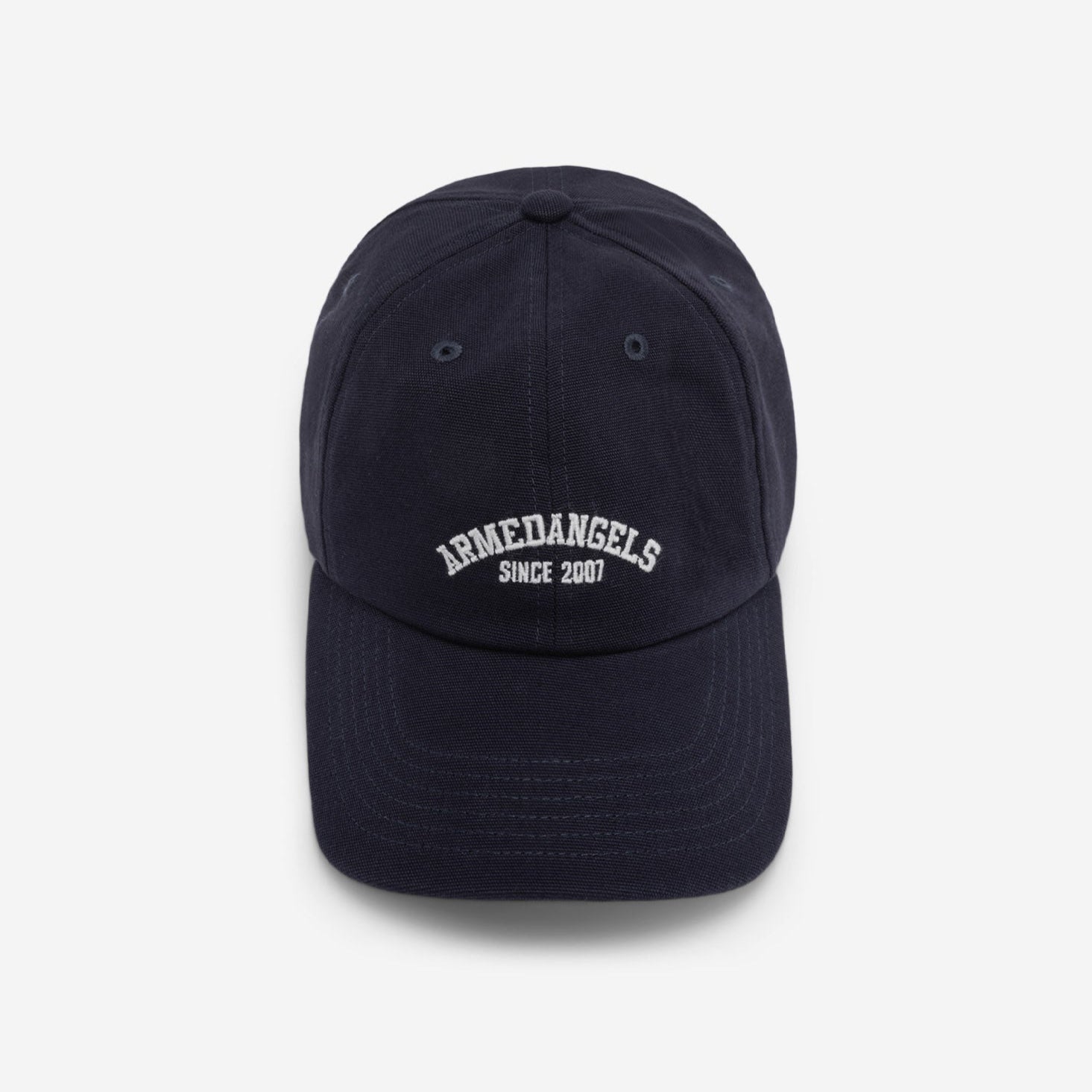 Eine marineblaue Baseballmütze mit weißem gesticktem Text, der auf der Vorderseite ARMDANGELS SINCE 2007 lautet, auf einem schlichten hellgrauen Hintergrund.