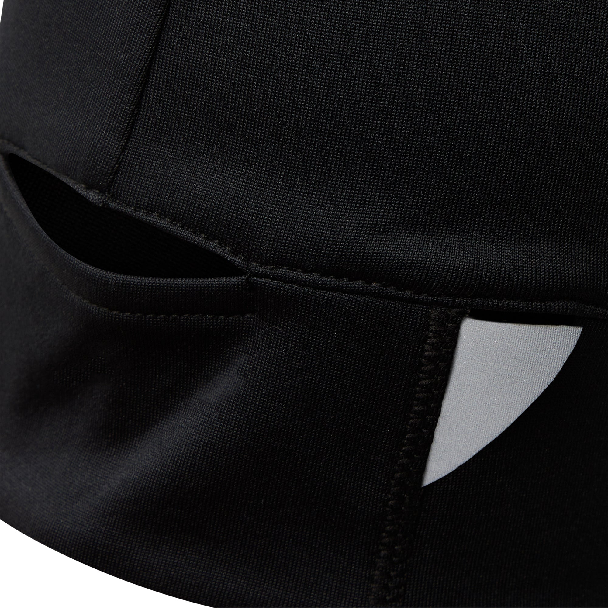 Nahaufnahme einer schwarzen Stoffmütze mit einem horizontalen Schlitz und einem kleinen weißen reflektierenden Aufnäher, der Nähte und Texturdetails zeigt.