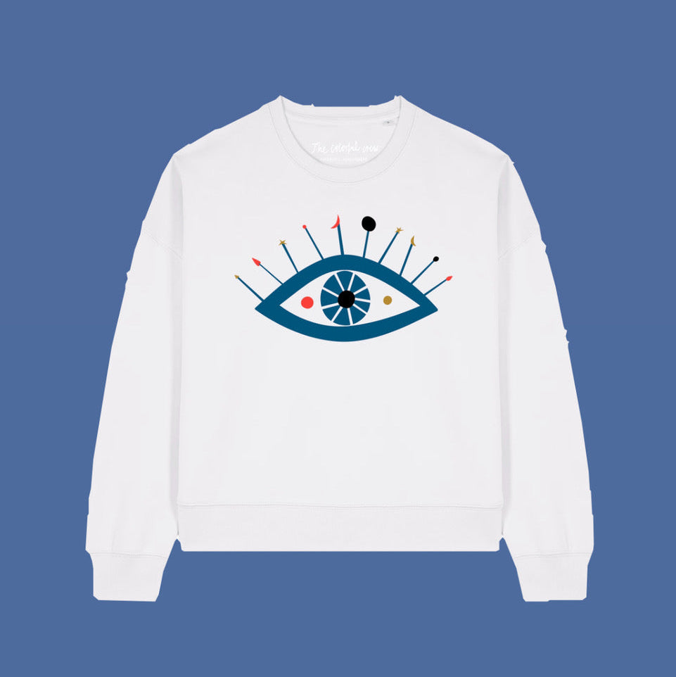 Ein weißes Sweatshirt mit einer stilisierten blauen Augengrafik auf der Vorderseite. Das Auge hat bunte Linien und Punkte, die von der Spitze ausstrahlen, auf einem einfarbig blauen Hintergrund.