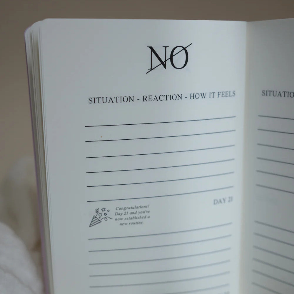 Ein aufgeschlagenes Tagebuch zeigt eine Seite mit der Überschrift "NEIN" mit den Rubriken "SITUATION - REAKTION - WIE ES SICH ANFÜHLT" und linierten Feldern zum Schreiben. Auf der Seite steht auch "TAG 21" und eine kleine Glückwunschnachricht mit einem Symbol.