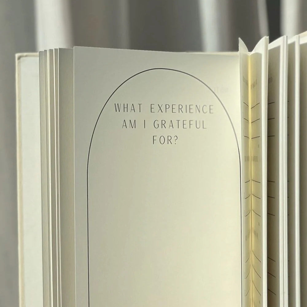 Ein aufgeschlagenes Tagebuch mit der Aufforderung "Wofür bin ich dankbar?" auf einer leeren Seite, mit sanftem natürlichem Licht, das das Papier beleuchtet, und einer gewebten Oberfläche unter dem Tagebuch.