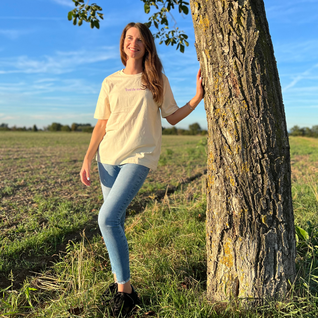 Eine Frau steht neben einem Baum auf einem Feld bei sonnigem Wetter.