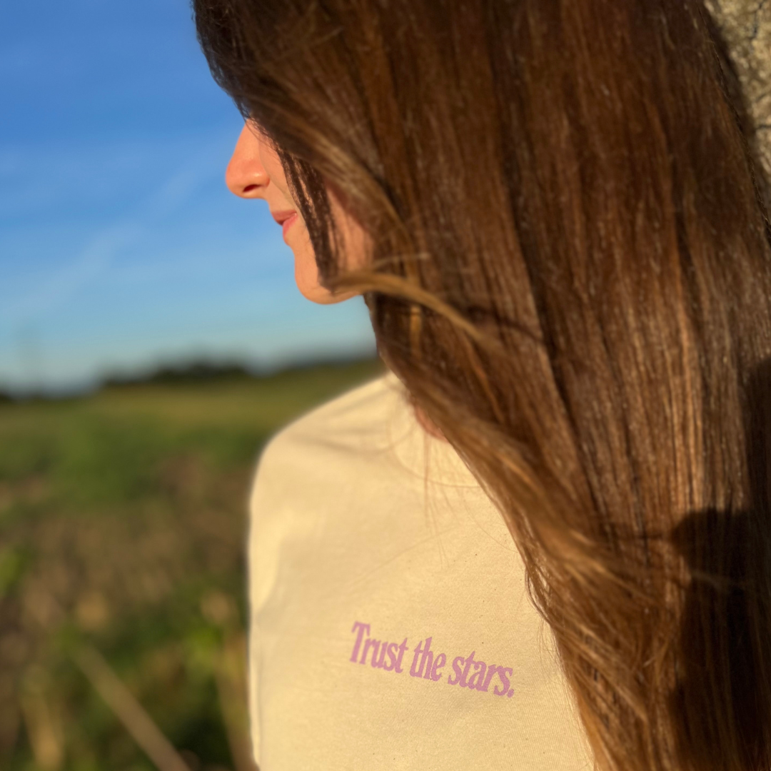 Frau im Profil, steht im Sonnenschein auf einem Feld, trägt ein Shirt mit der Aufschrift "Trust the stars".