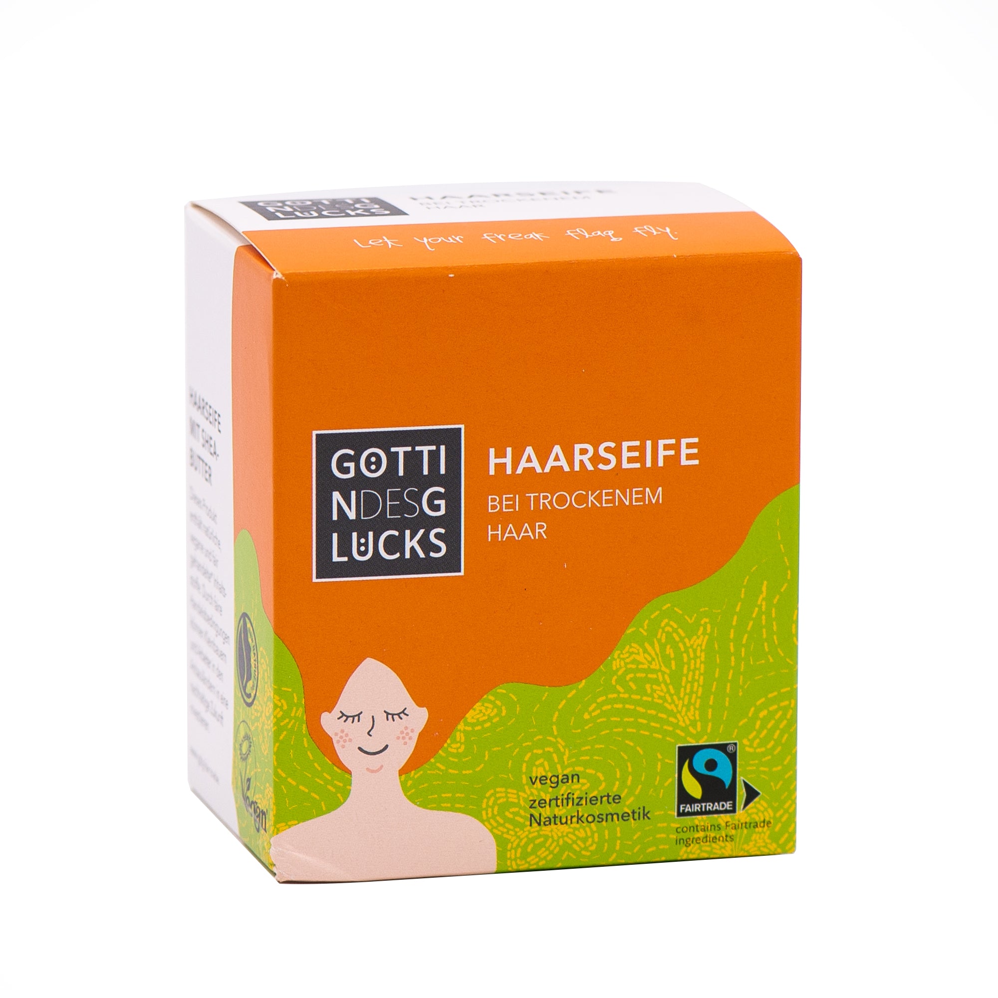 Orangefarbene und grüne Schachtel des festen Shampoos "Göttin des Glücks" für trockenes Haar, mit einer einfachen Strichzeichnung einer Frau, Fairtrade- und Vegan-Logos und einem deutschen Text, der das Produkt als Naturkosmetik beschreibt.