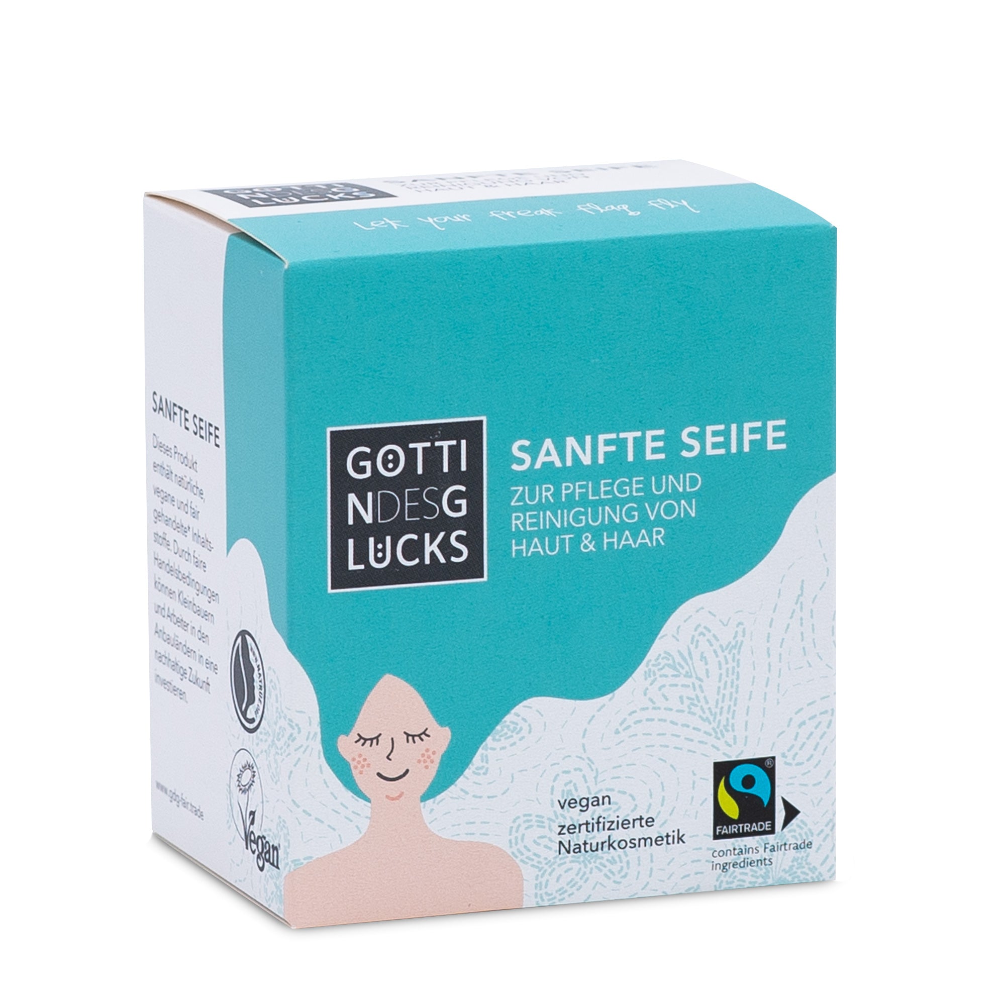 Eine Schachtel mit der sanften Seife Göttin des Glücks Sanfte Seife, mit der Illustration einer lächelnden Frau, Wellen und Zertifizierungen für vegane, natürliche Kosmetik und Fairtrade. Der Text auf Deutsch wirbt für Haut- und Haarpflege.