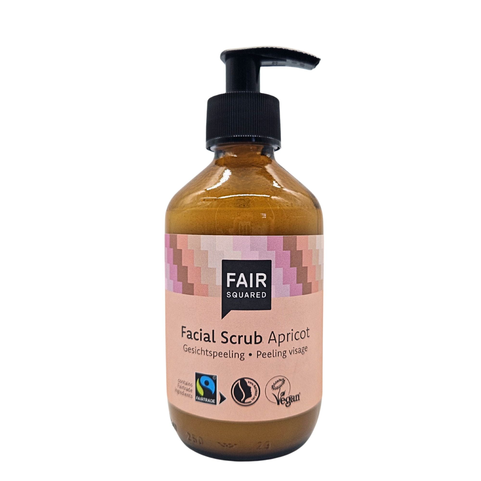 Eine braune Pumpflasche mit der Aufschrift Fair Squared Facial Scrub Apricot und den Logos der Fairtrade-, Vegan- und Halal-Zertifizierung. Das Etikett hat oben ein rosafarbenes geometrisches Muster und Text in Englisch und Deutsch.