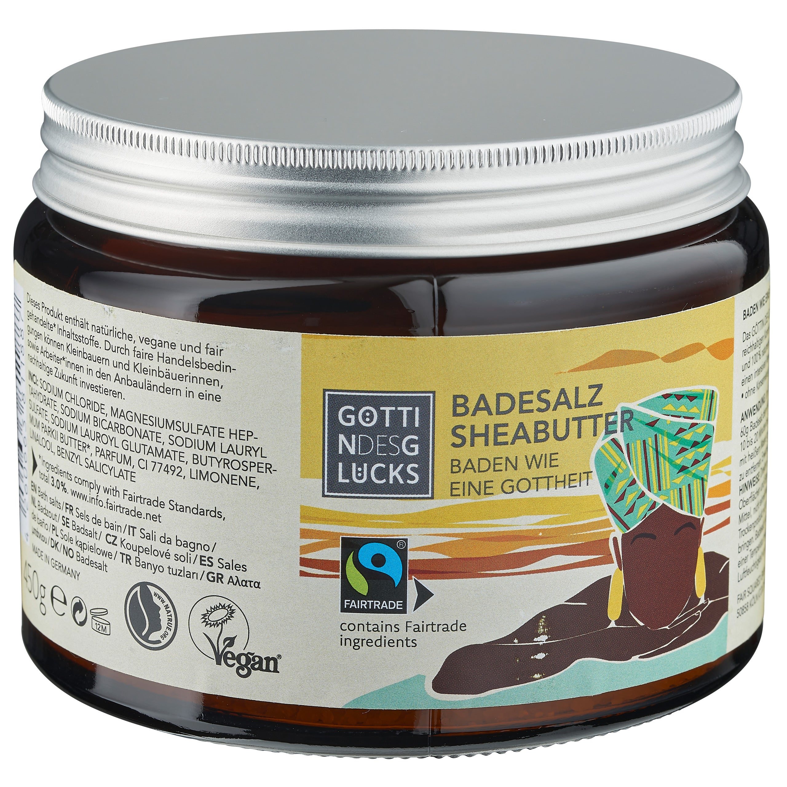 Eine braune Dose Badesalz mit der Aufschrift Badesalz Sheabutter und der Abbildung einer Frau in farbenfroher Kleidung und Kopfbedeckung. Auf der Verpackung sind die Logos für Vegan und Fairtrade zu sehen. Der Text ist auf Deutsch.