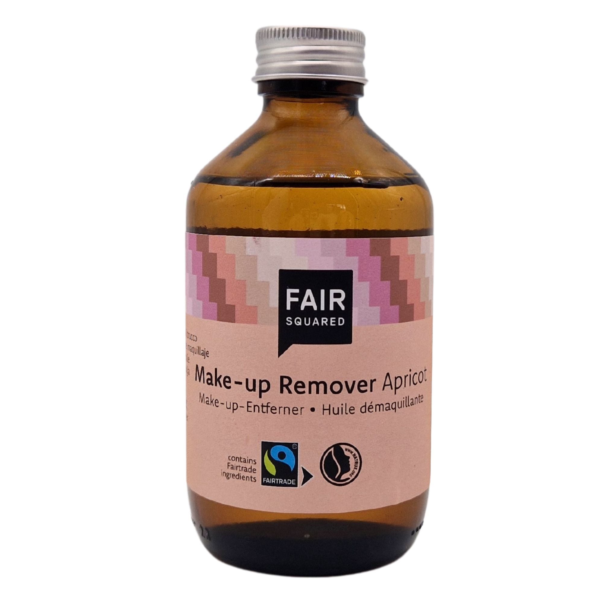 Eine braune Glasflasche mit der Aufschrift FAIR SQUARED Make-up Remover Apricot, mit Fairtrade- und Vegan-Logo, mit einem rosa, beige und lila gemusterten Etikett und einem silbernen Schraubverschluss.