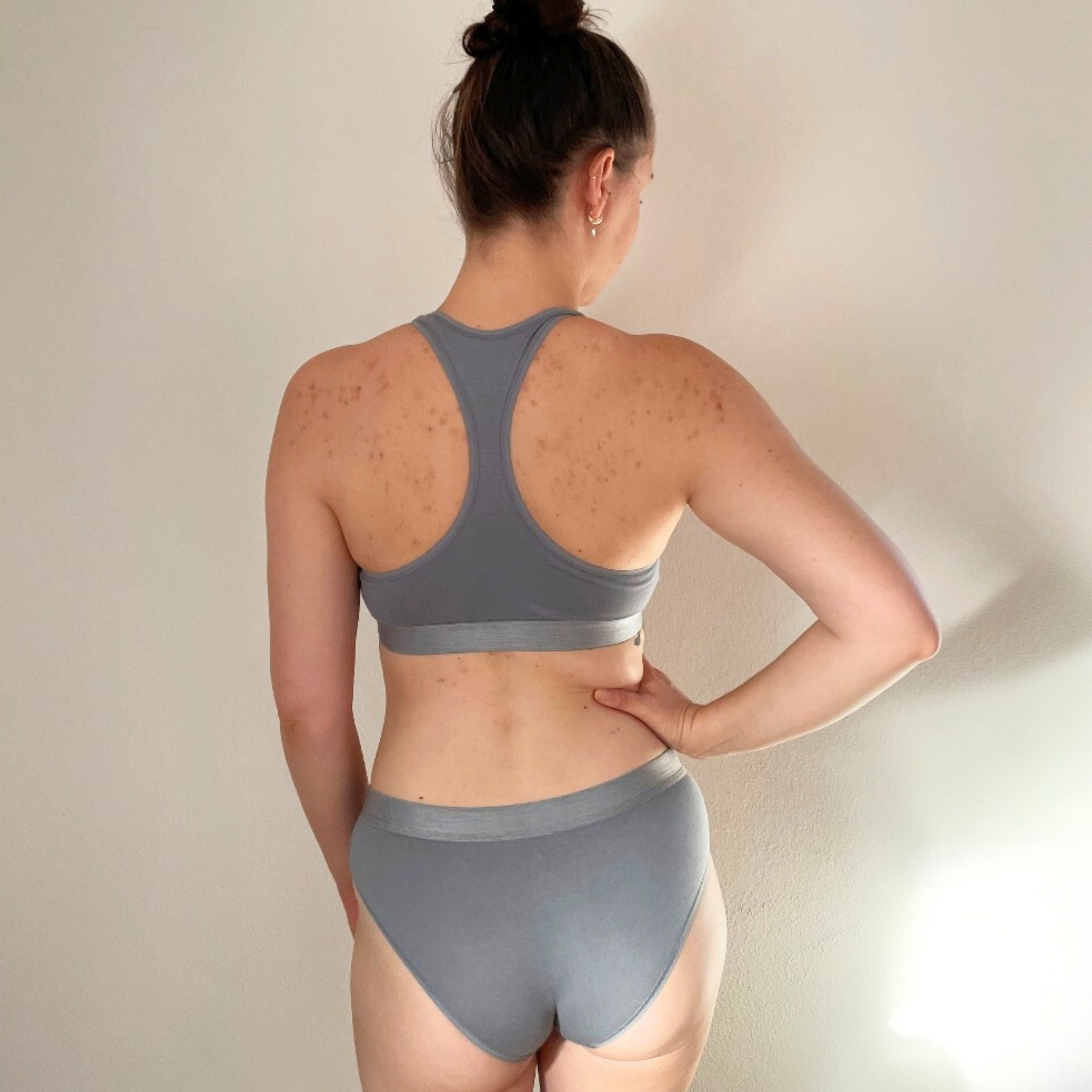 Rückansicht einer Person in grauer Sportbekleidung vor einer beigen Wand.