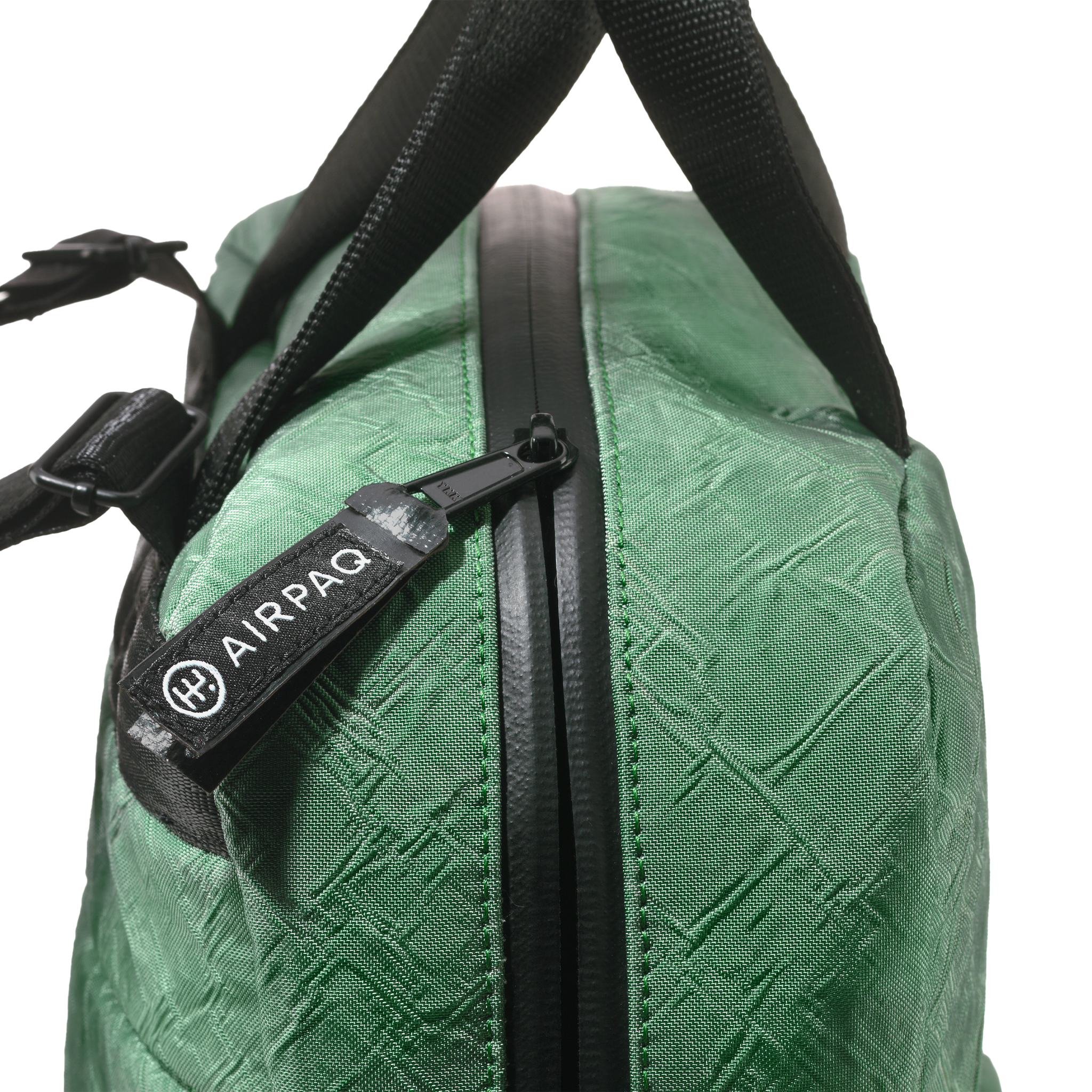 Nahaufnahme einer grünen Tasche mit schwarzem Reißverschluss und Griff. Auf dem Reißverschlussanhänger steht AIRPAQ mit einem runden Logo. Das Material der Tasche hat ein strukturiertes, kreuzförmiges Muster.