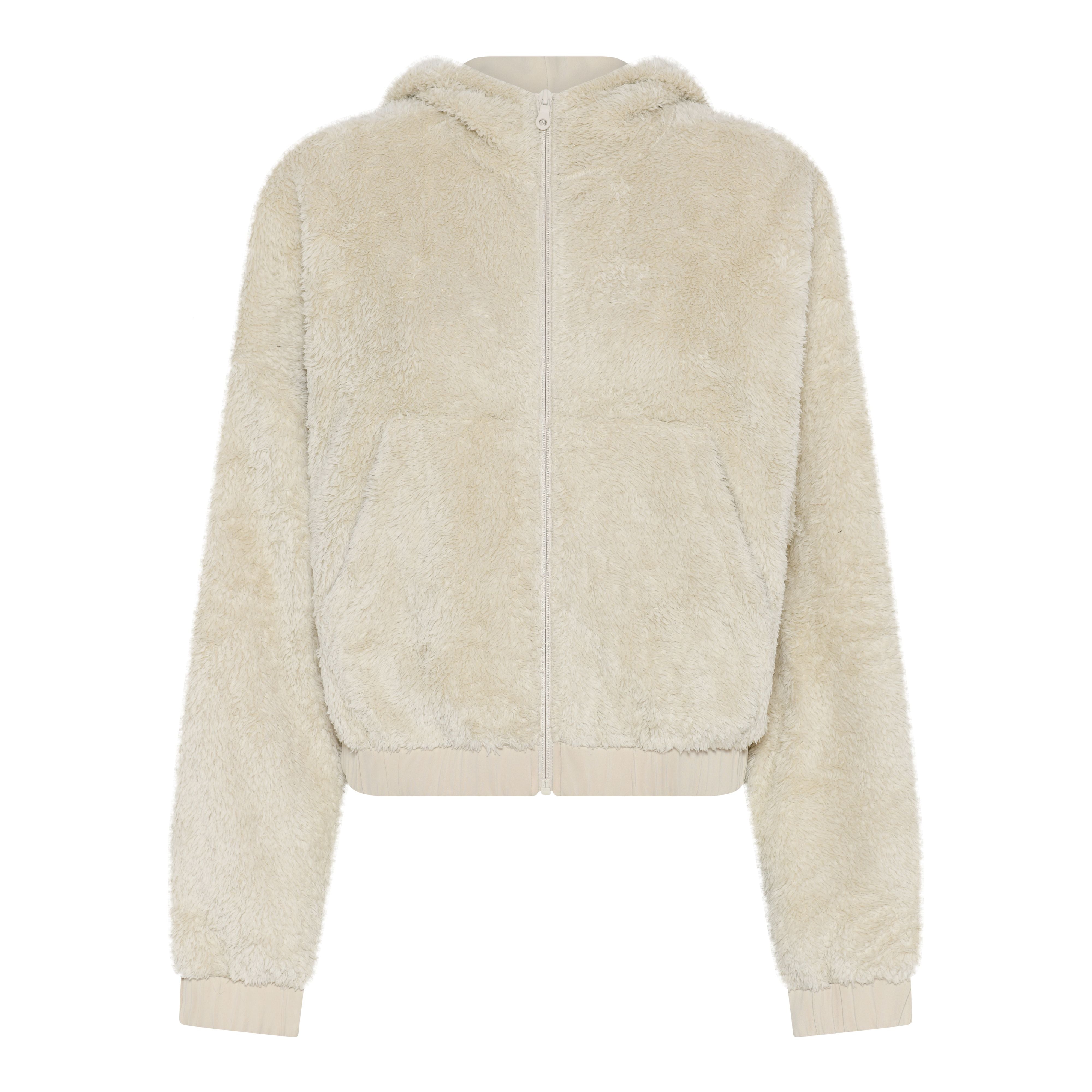 Eine cremefarbene Kapuzenjacke mit Reißverschluss aus weichem, plüschigem Fleecestoff, mit Vordertaschen und gerippten Bündchen und Saum. Die Jacke ist auf einem einfarbig weißen Hintergrund abgebildet.